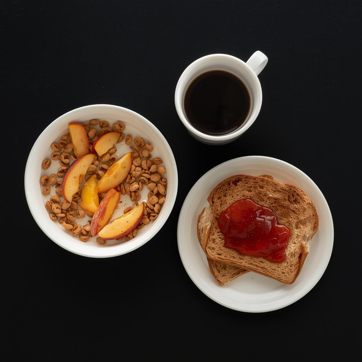 Breakfast spread with cereal and peach slices, toast with jam, and a cup of black coffee on a dark background