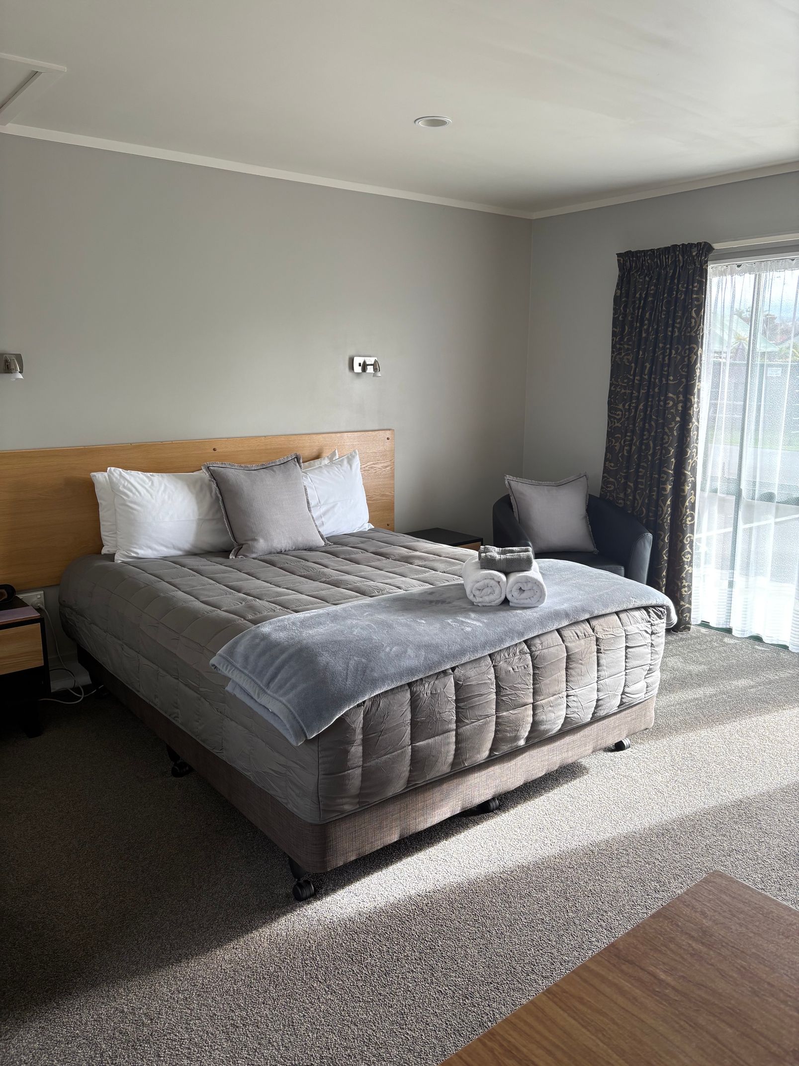 Neatly made bed in a gray bedroom with a large window and sheer curtains.