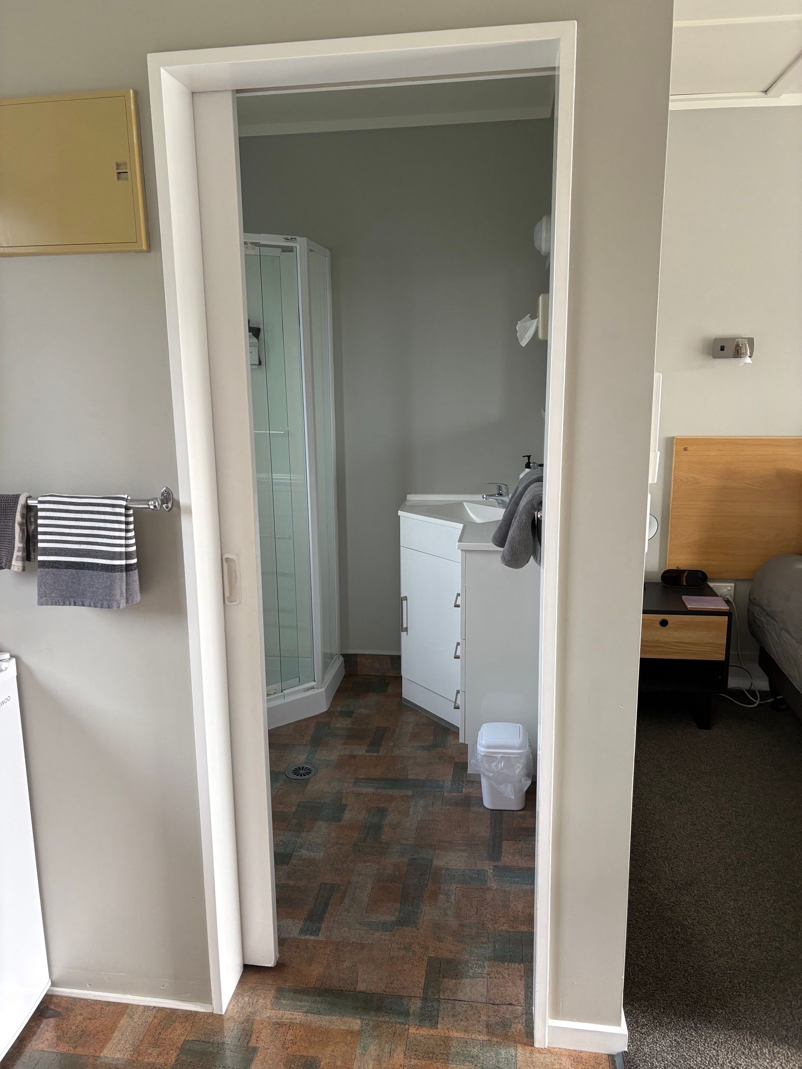 View through a doorway into a small bathroom with a shower curtain, sink cabinet, and tile floor.