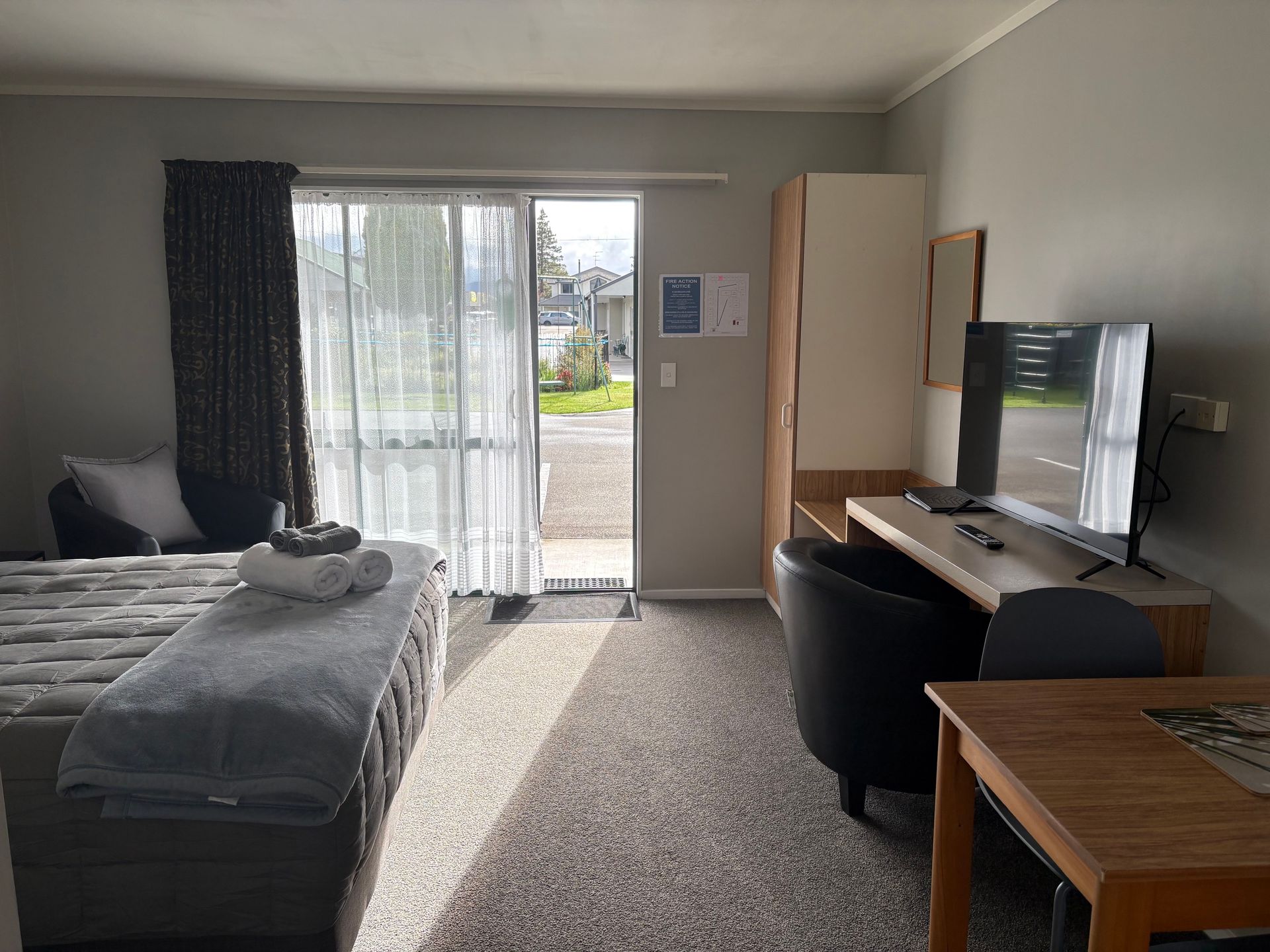 Small bedroom with bed, desk, TV, chair, and sliding glass door to a balcony.
