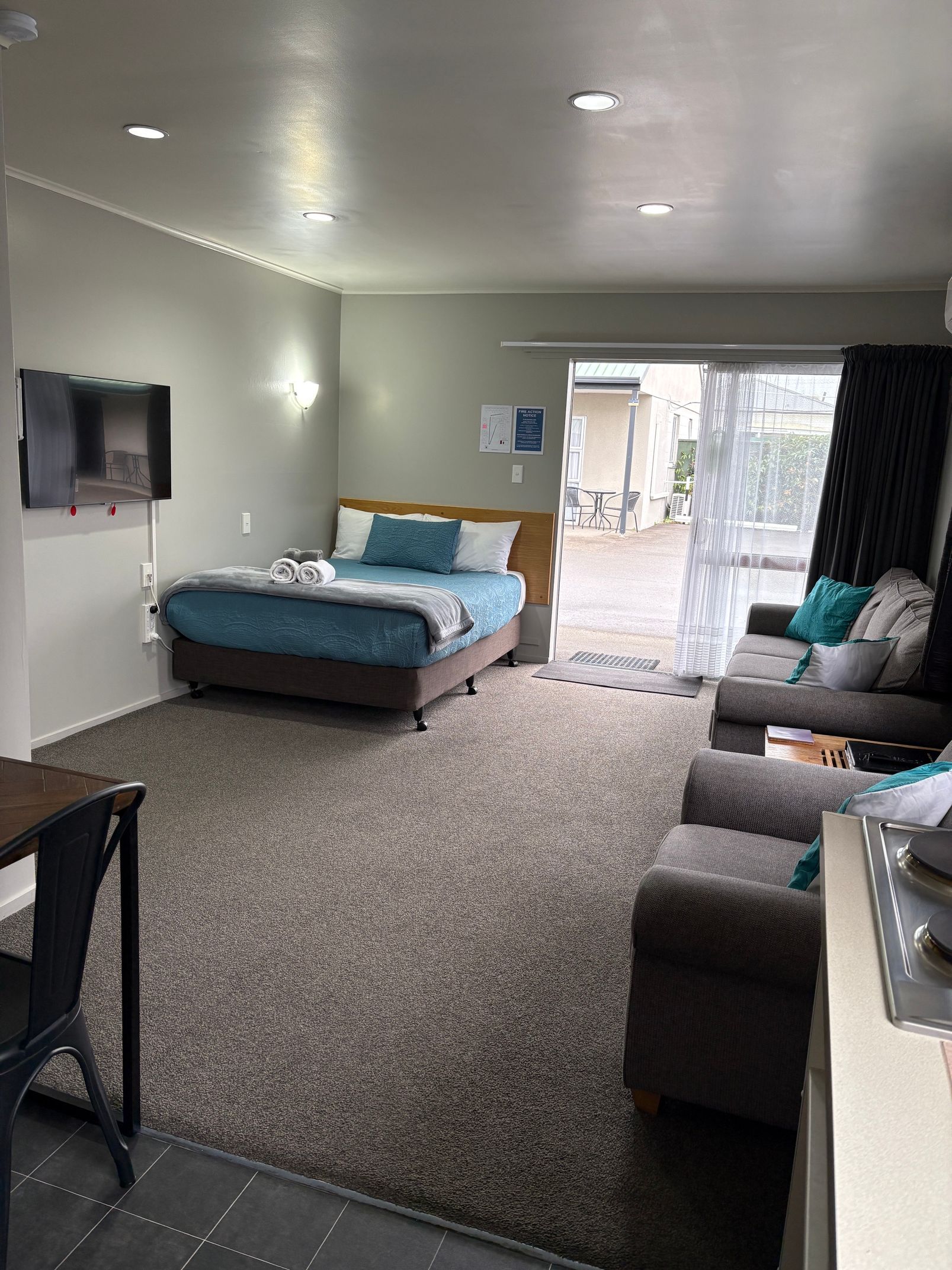 Modern studio room with bed, sofa, wall-mounted TV, and open door to a patio