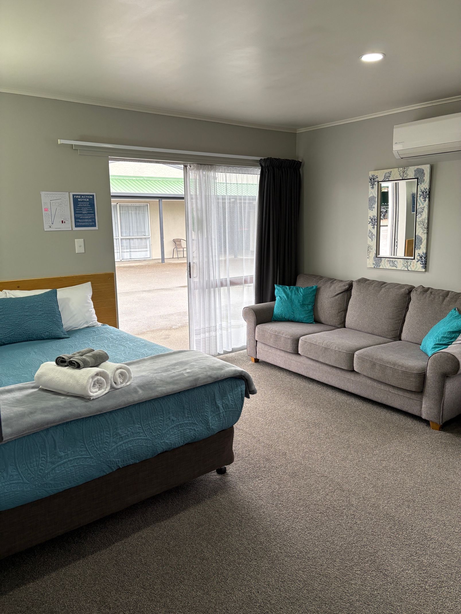 Bedroom with a teal bed, gray sofa, large mirror, and sliding glass door to a patio.