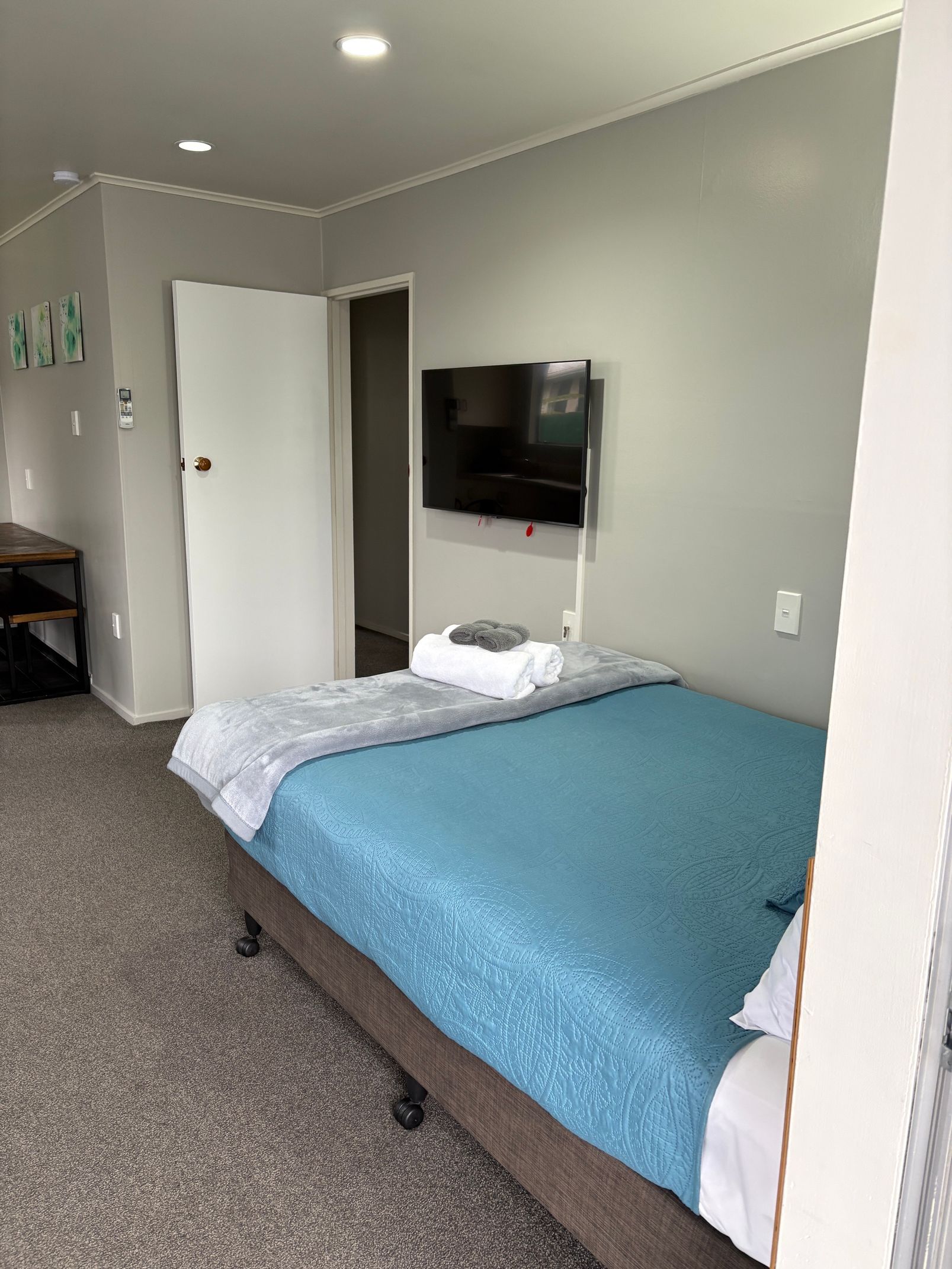 Bedroom with a bed, wall-mounted TV, open door, and gray carpet.