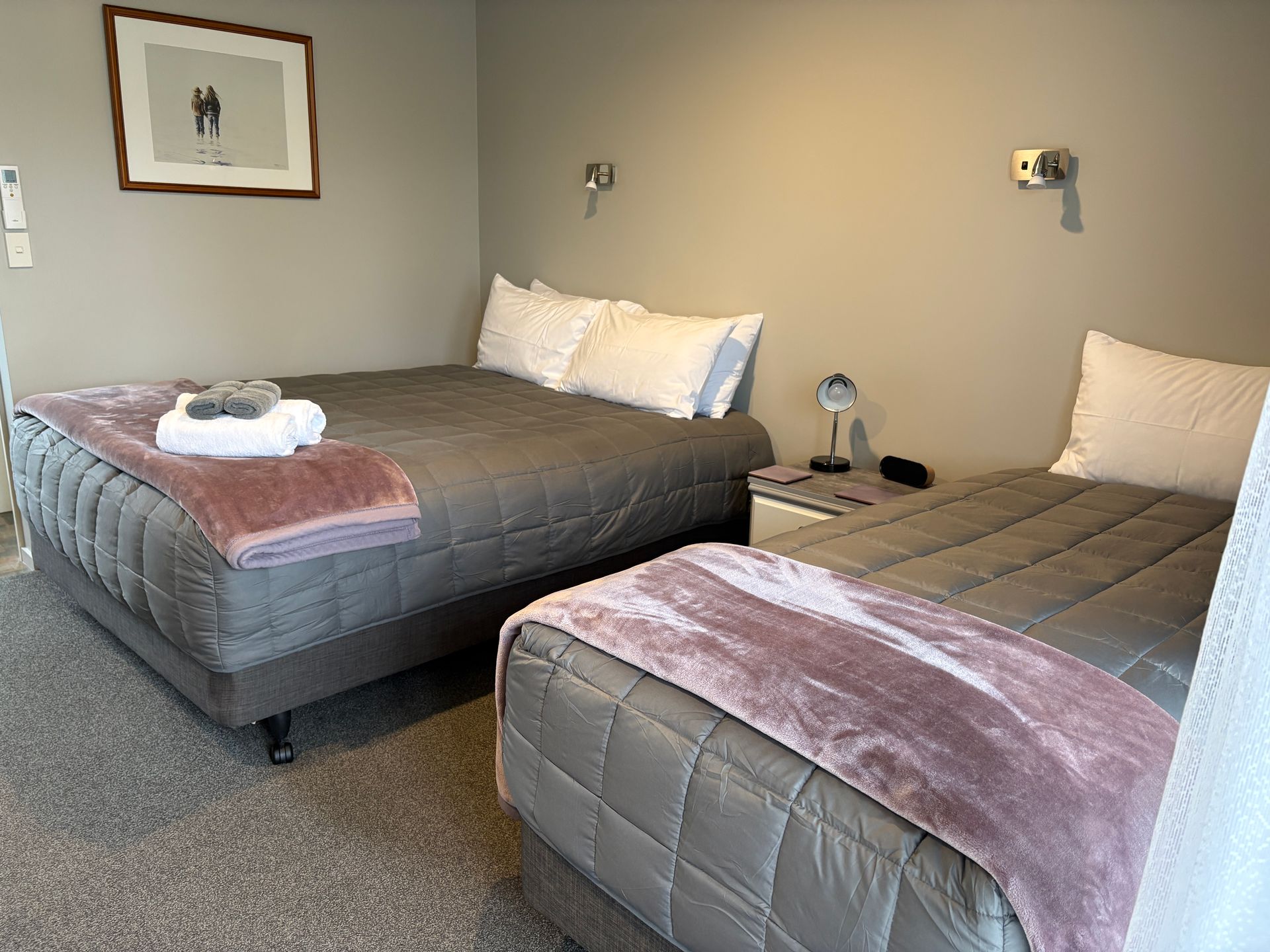 Hotel room with two gray beds, pink throws, bedside lamps, and framed wall art