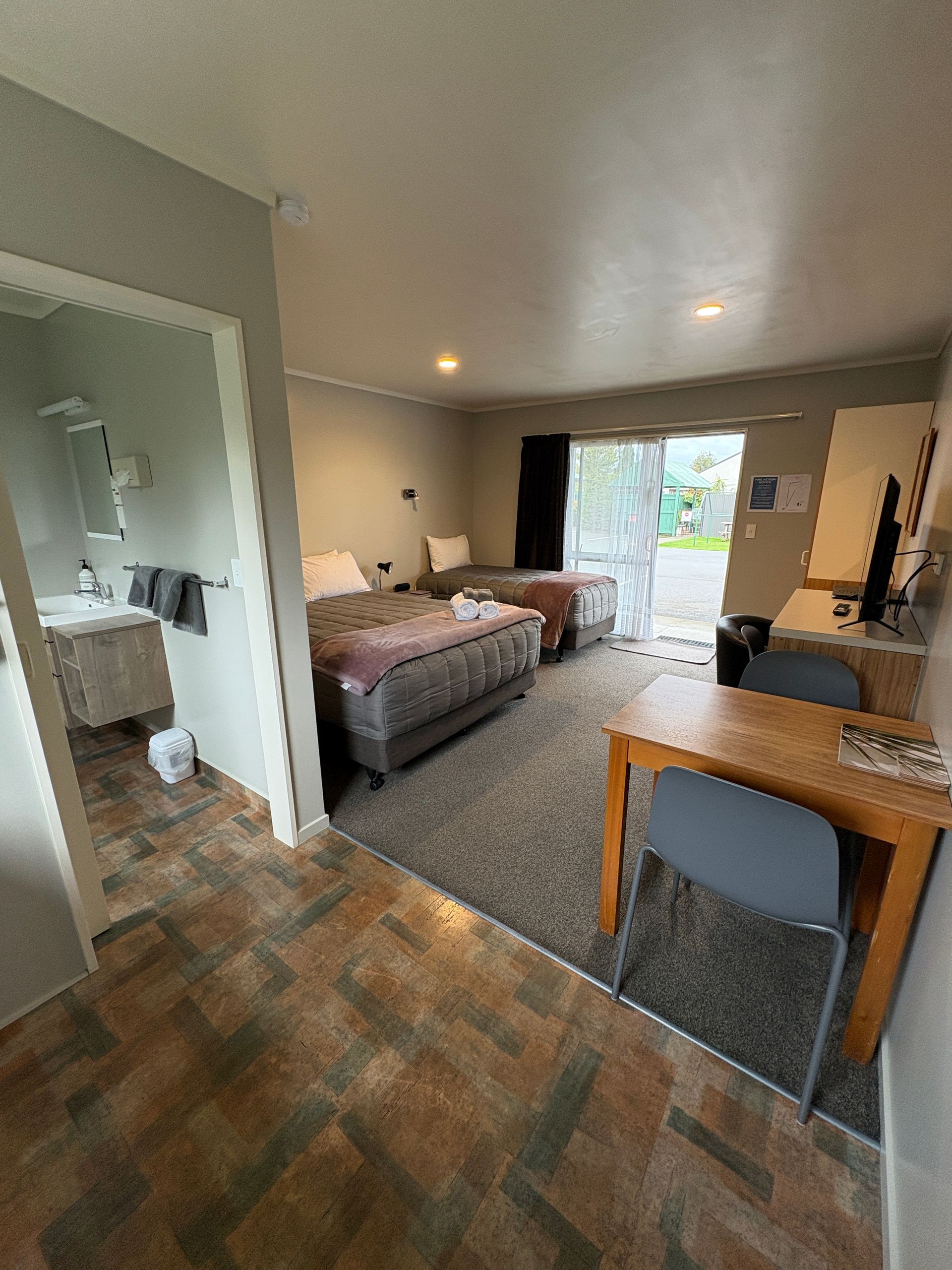 Hotel-style room with two twin beds, desk, bathroom doorway, and sliding glass door to a balcony.