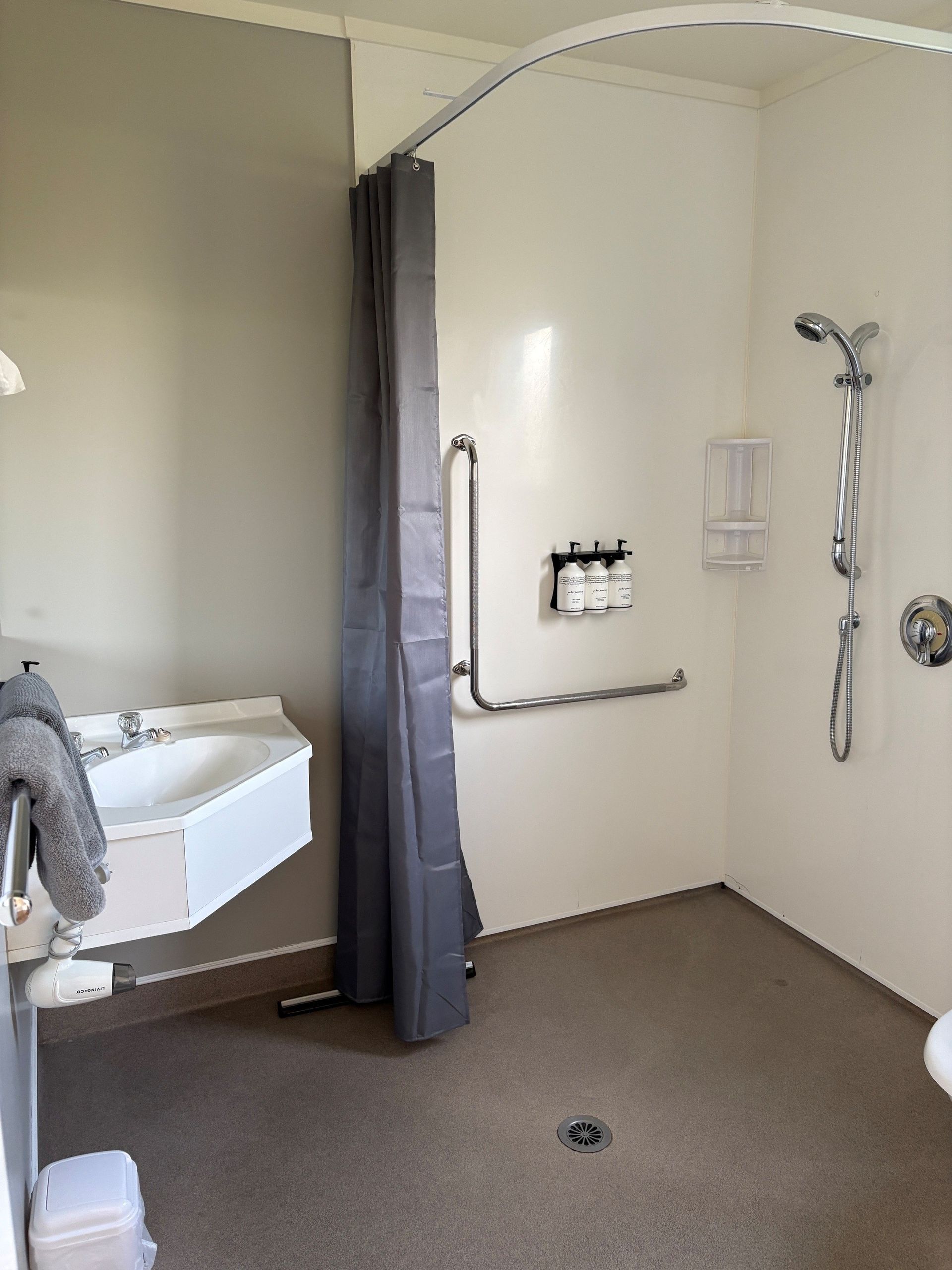 Accessible shower room with grab bars, handheld shower, sink, and roll-in floor drain