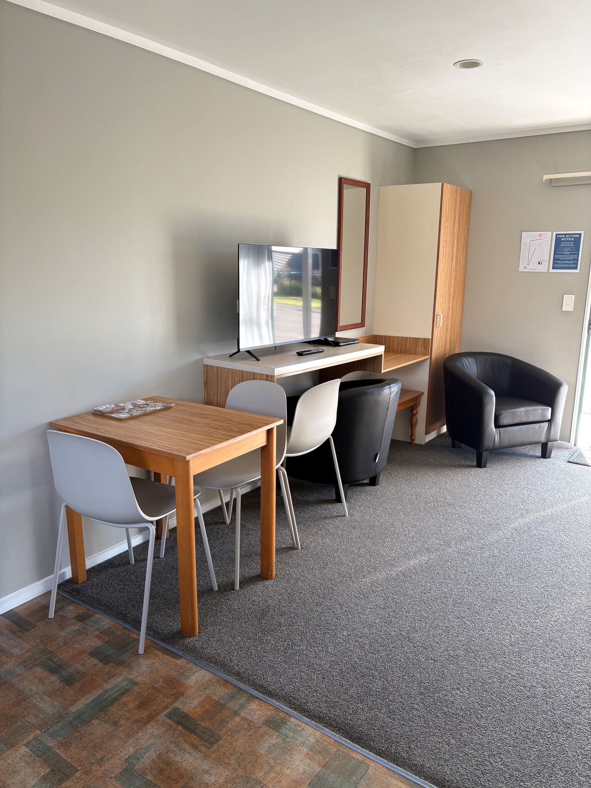 Small furnished room with two desks, a mirror, folding screen, and two black chairs on carpet.