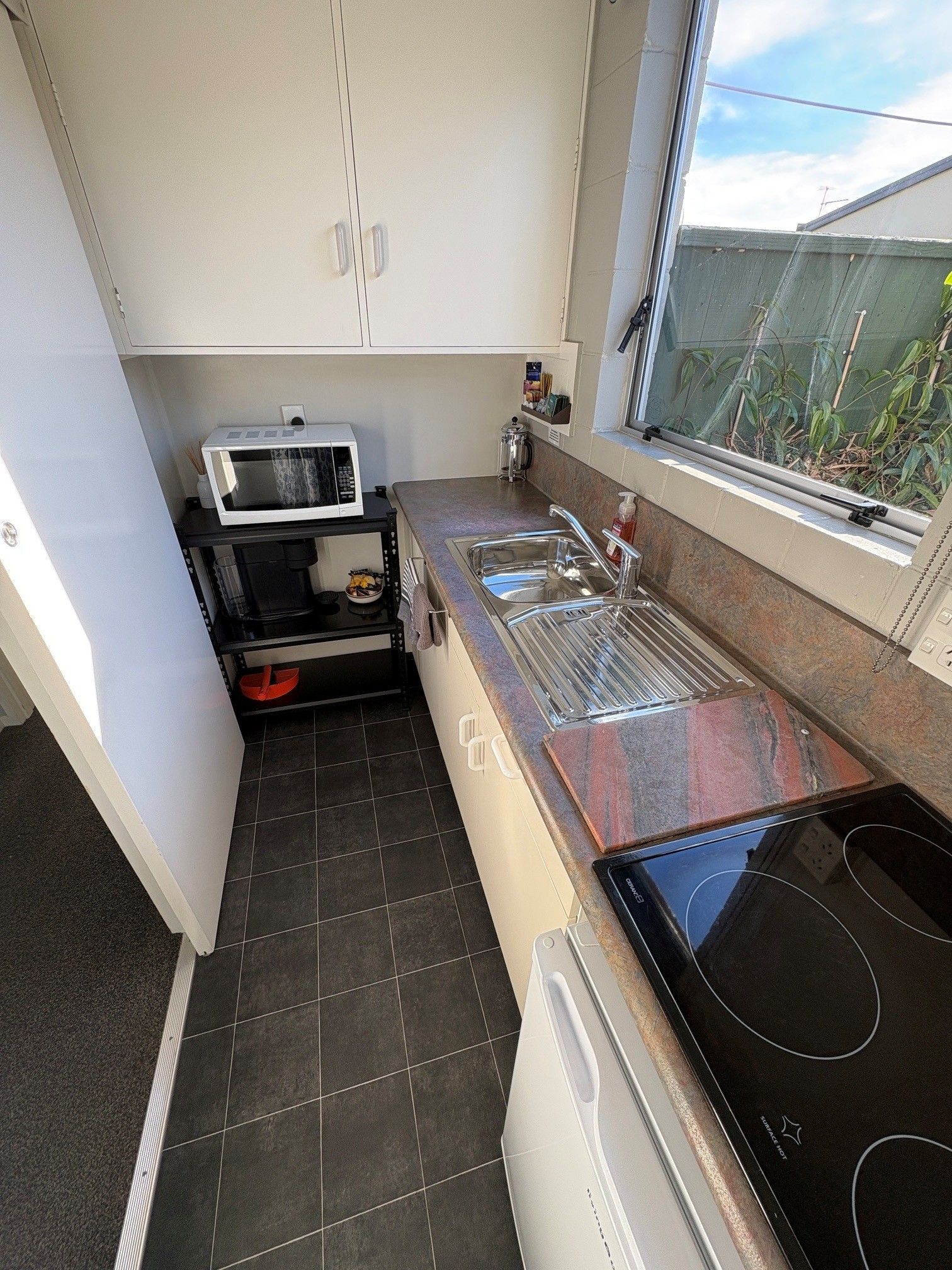 Narrow kitchen with sink, microwave, cabinets, and a large window beside a black countertop.