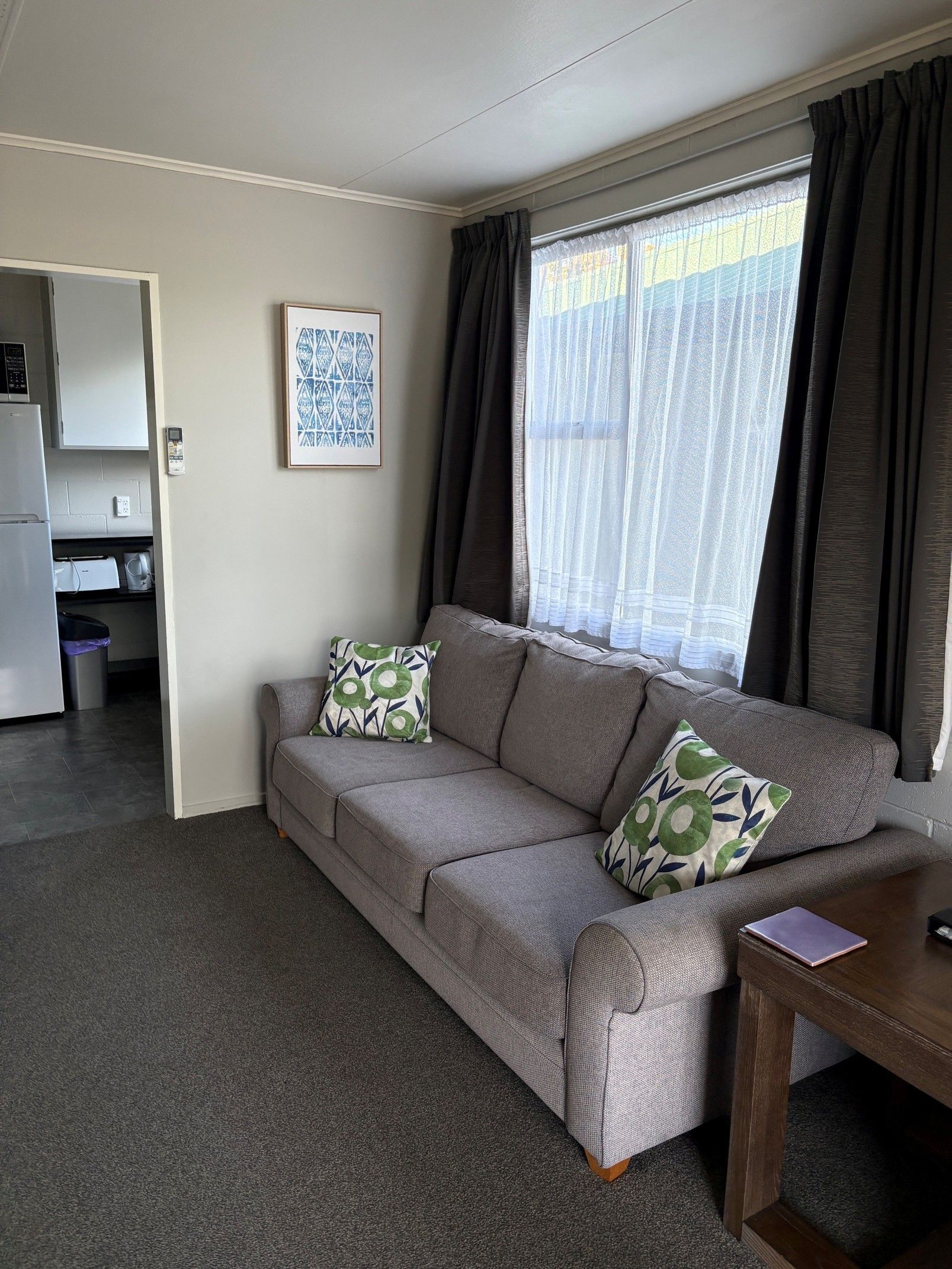 Living room with a gray sofa, patterned cushions, window curtains, and a small side table