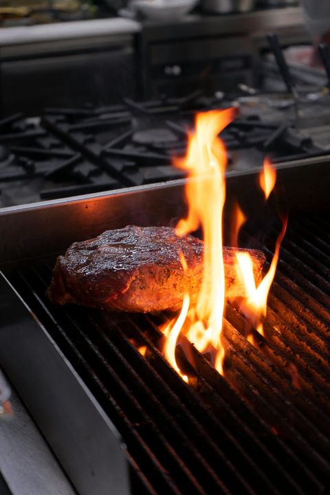 Steak grilling over open flames on a barbecue grate in a kitchen