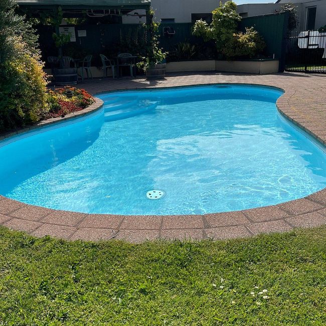 Backyard swimming pool with bright blue water, stone edge, and green lawn in the foreground