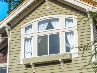 Green house with large window, white trim, and arched top panes.