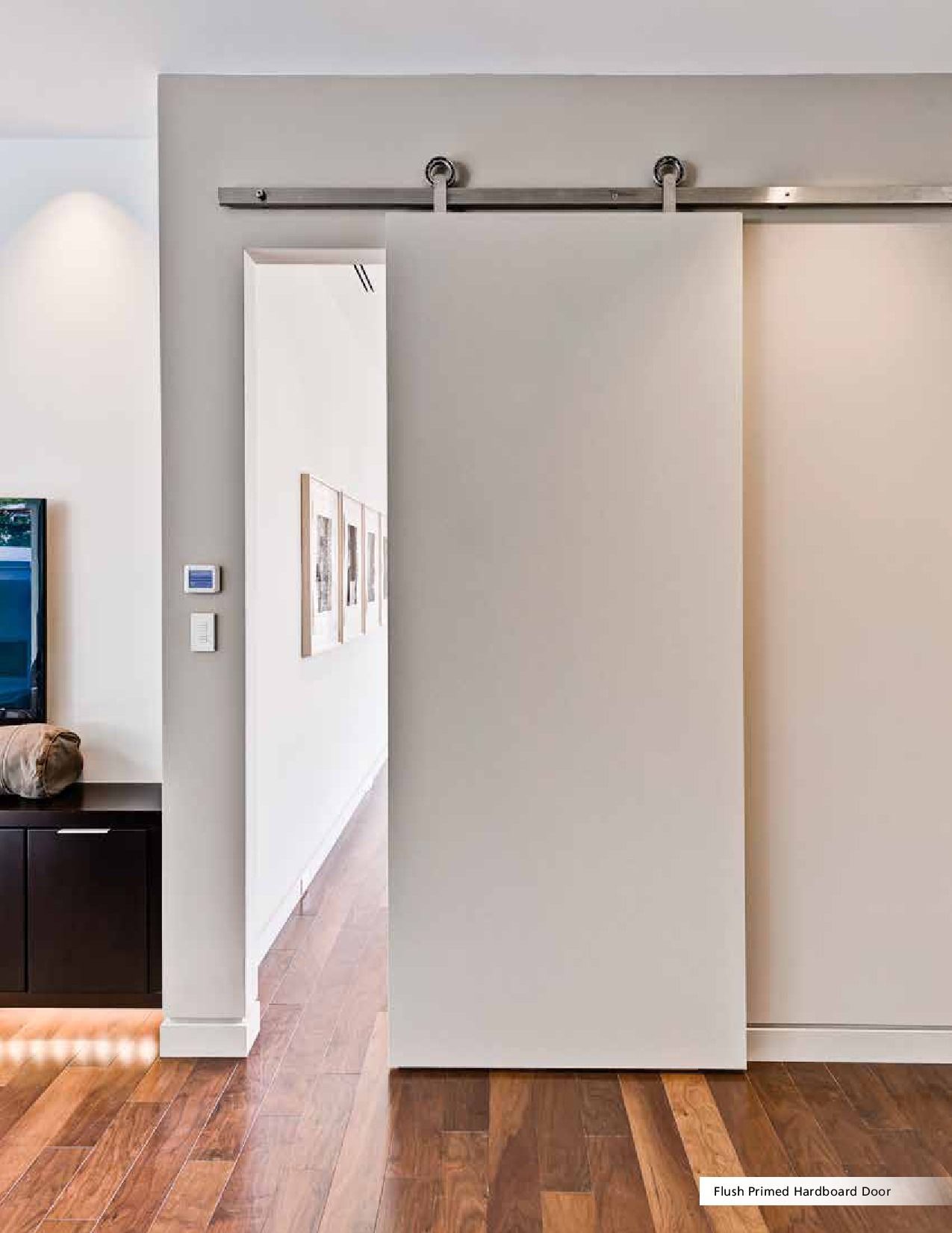 Modern sliding barn door, neutral color. Door open, revealing hallway with framed artwork and hardwood floor.