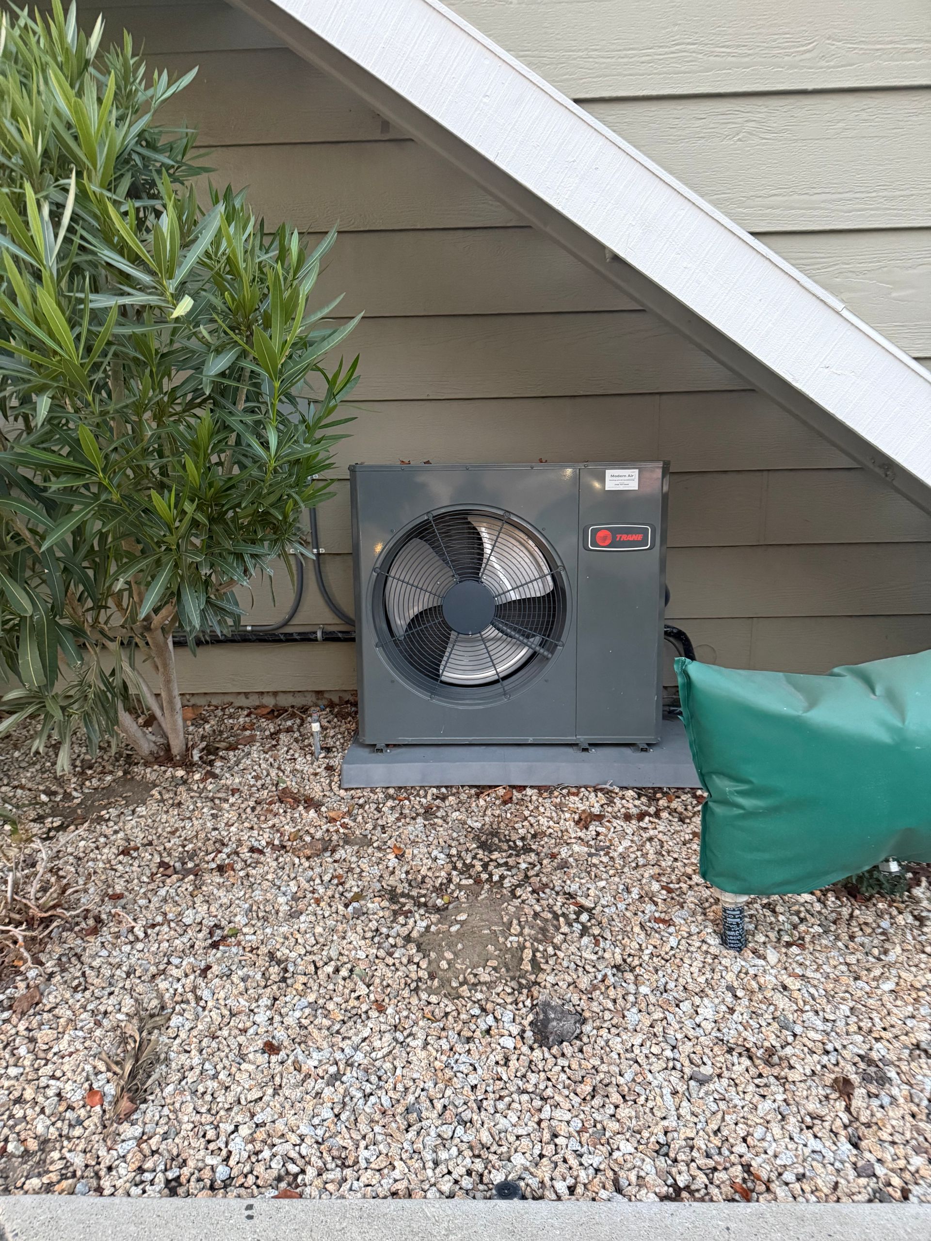 Technician repairing air conditioning unit, using tools near the condenser and refrigerant tanks.