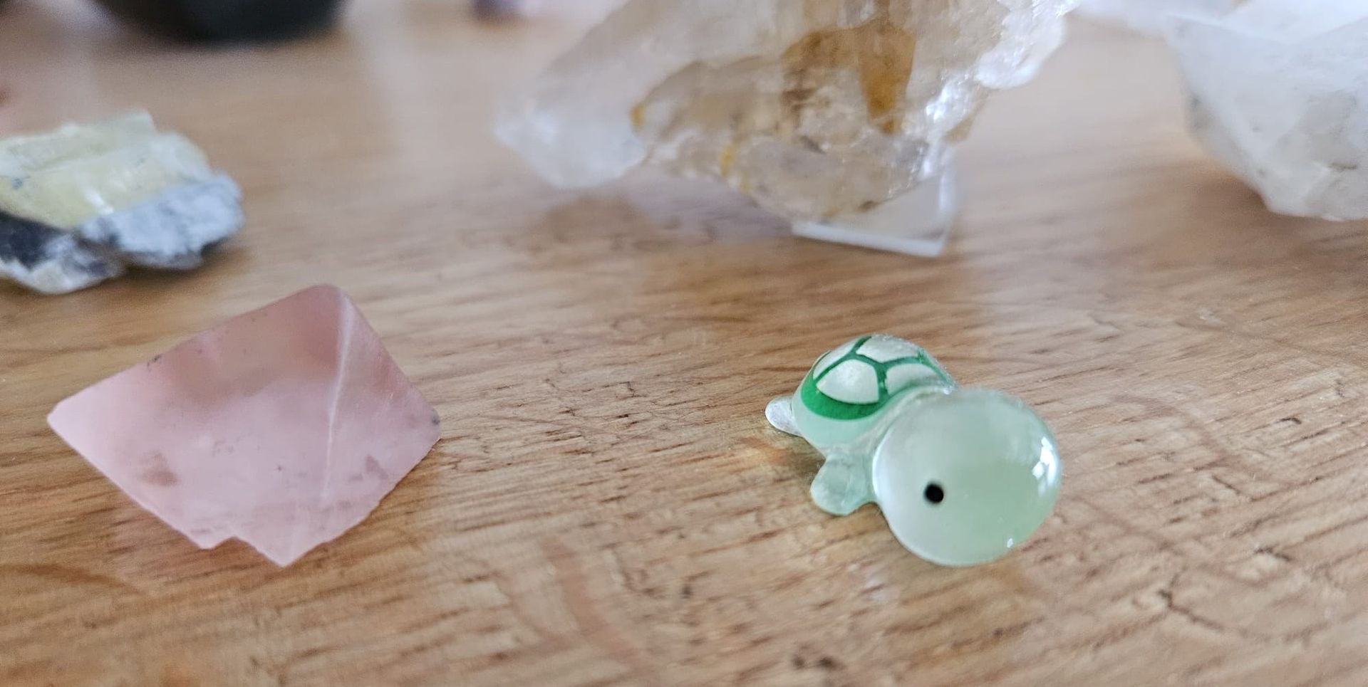 Kleine Kristallschildkrötenfigur neben rosa und klaren Kristallen auf einer Holzoberfläche