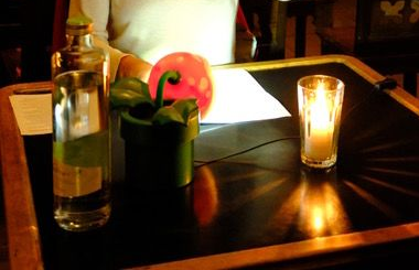 Ein mit Kerzen beleuchteter Tisch mit einer Glasflasche, einer grünen Pflanze und einer roten Schale in einem gedämpften Restaurantambiente