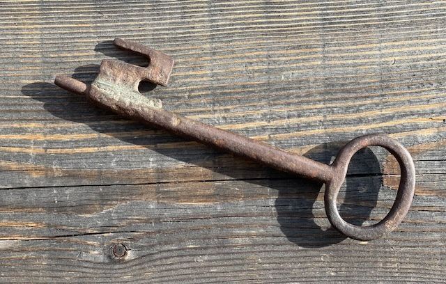Ein alter rostiger Schlüssel liegt auf einem Holztisch.