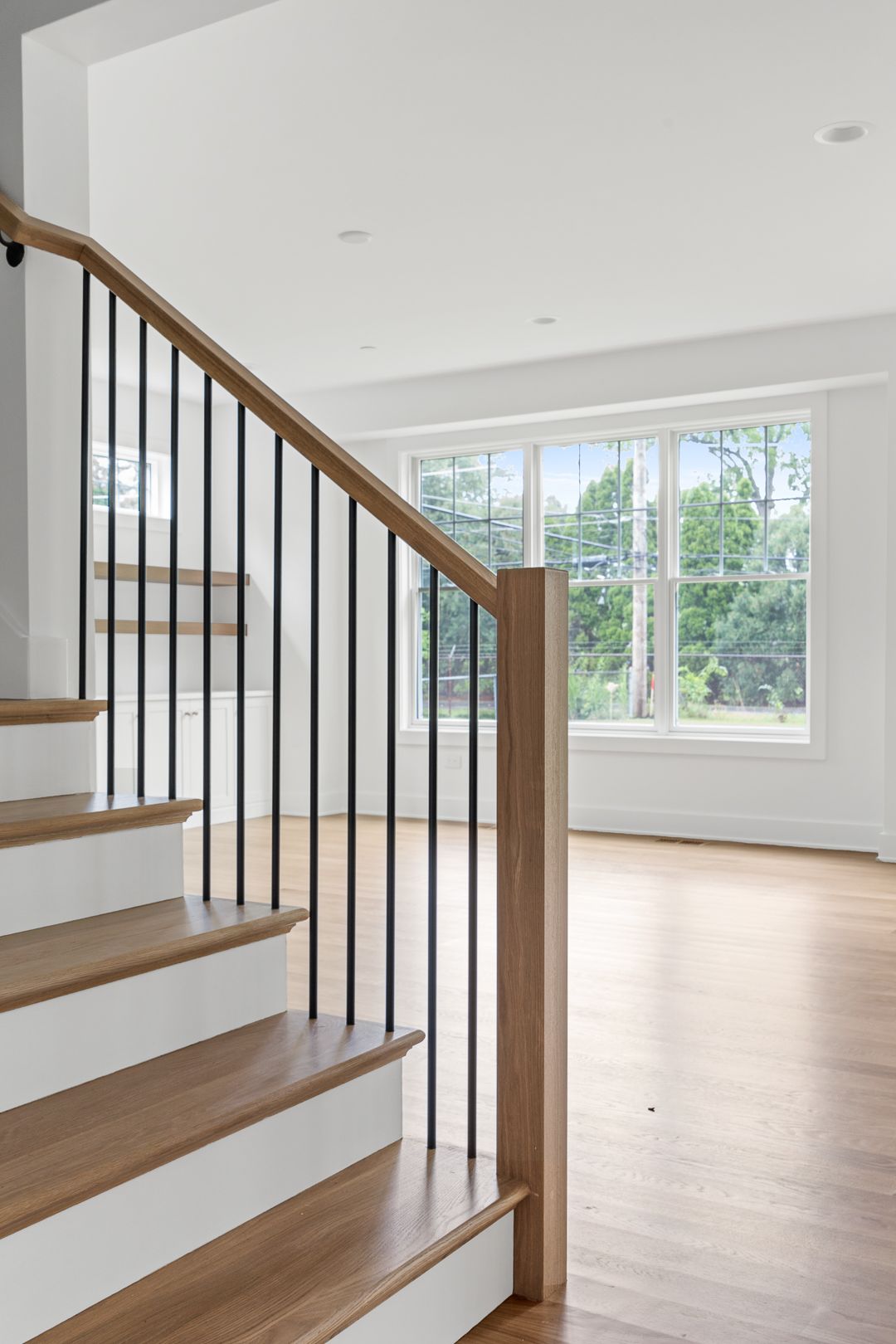 A wooden staircase with a metal railing in an empty room with a window.