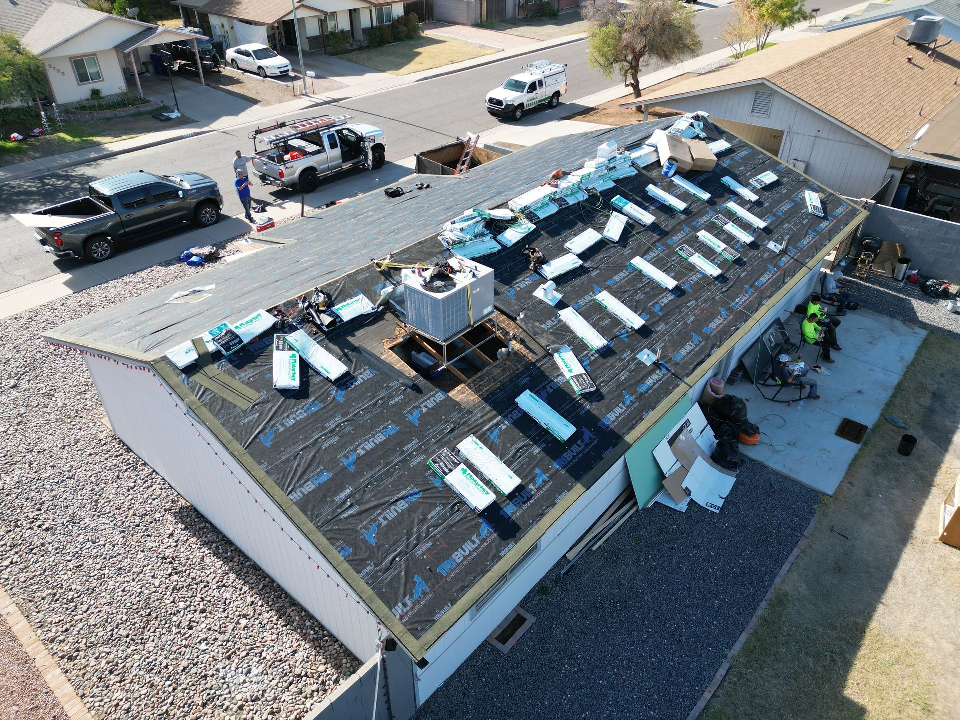 Aerial view of a roof under repair with roofing materials and workers in a residential neighborhood