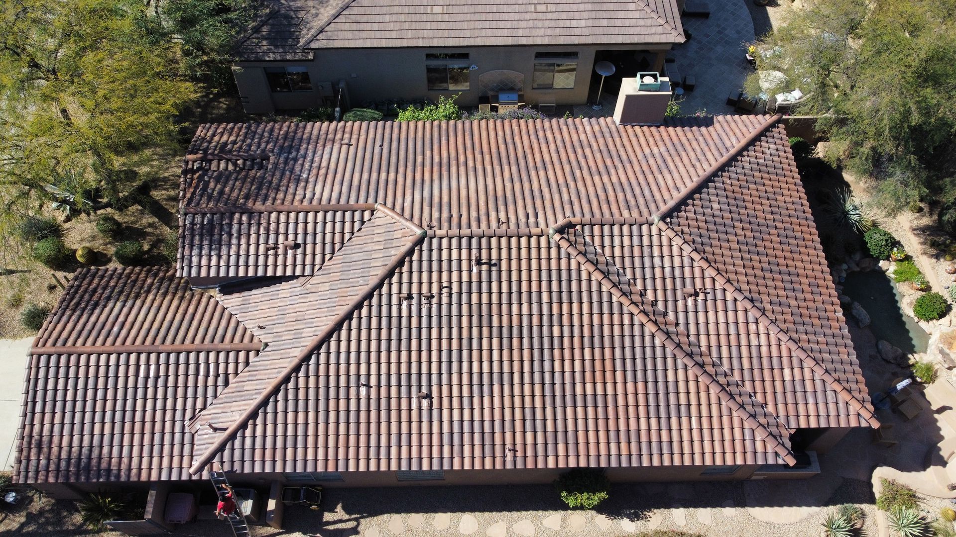 Aerial view of a house with a tan tiled roof and surrounding trees