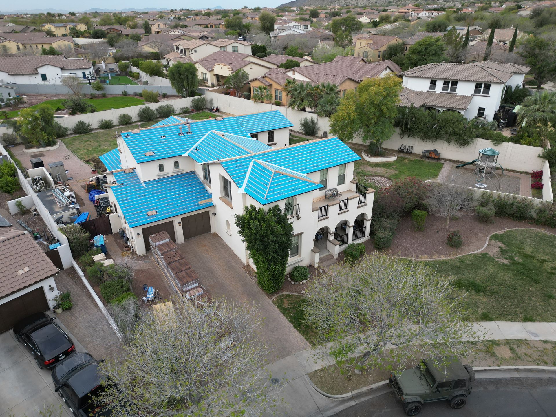 Aerial view of a large house with bright blue roof in a suburban neighborhood