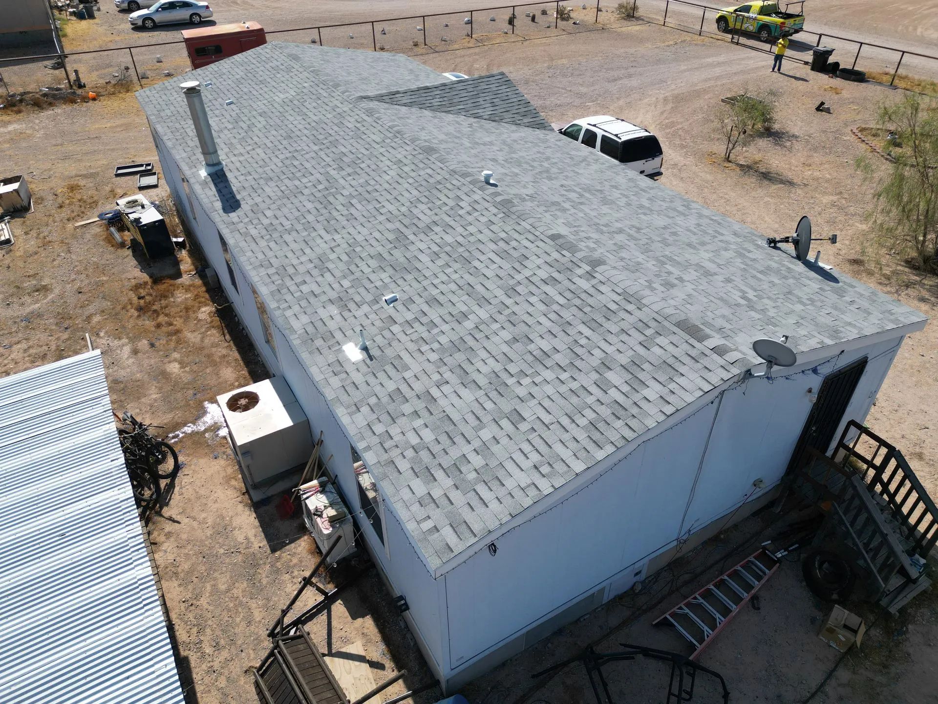 Aerial view of a gray-roofed building in a dry lot with vehicles and stairs nearby