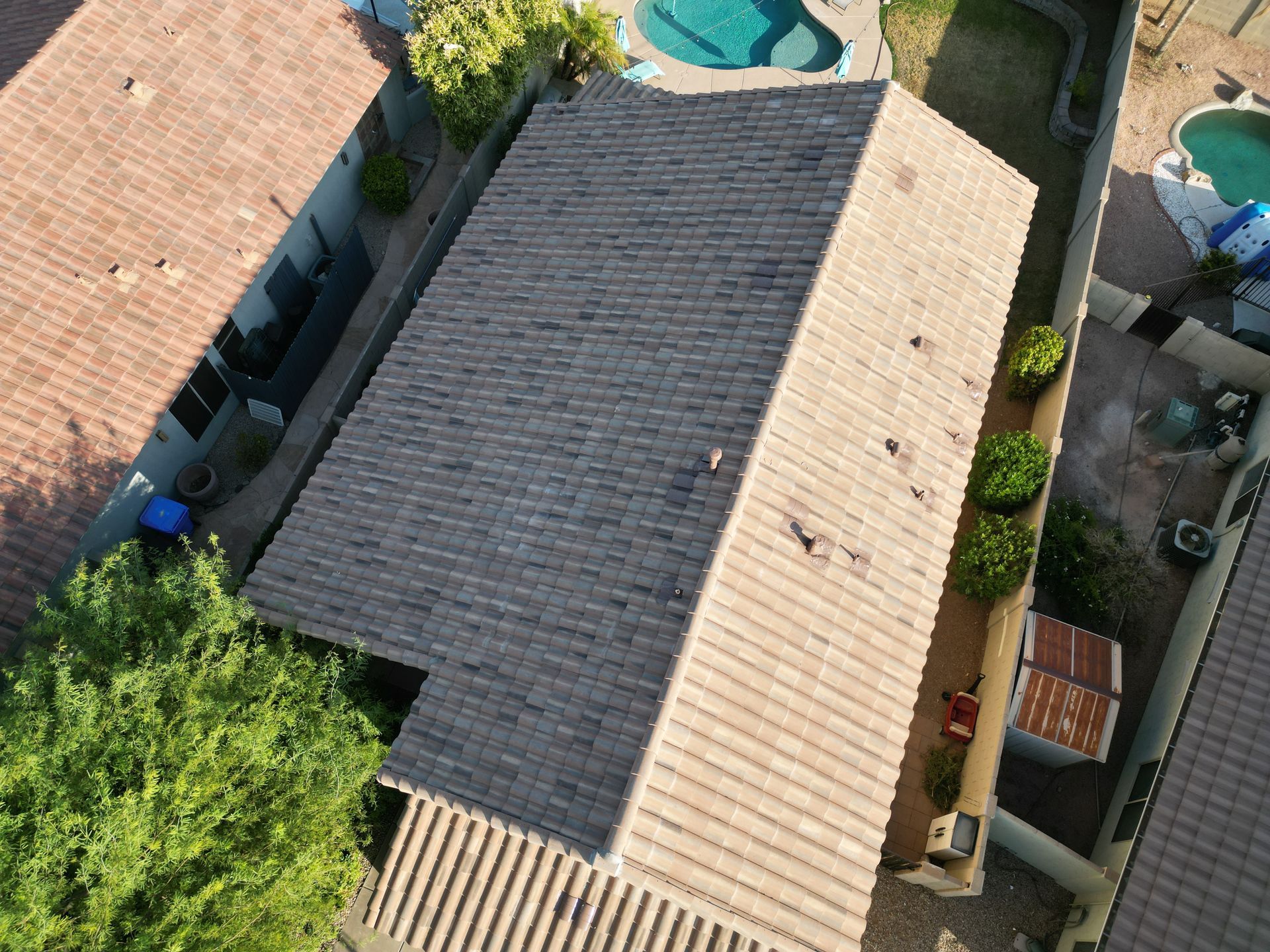 Aerial view of a house with a tan roof, surrounded by trees and neighboring homes.
