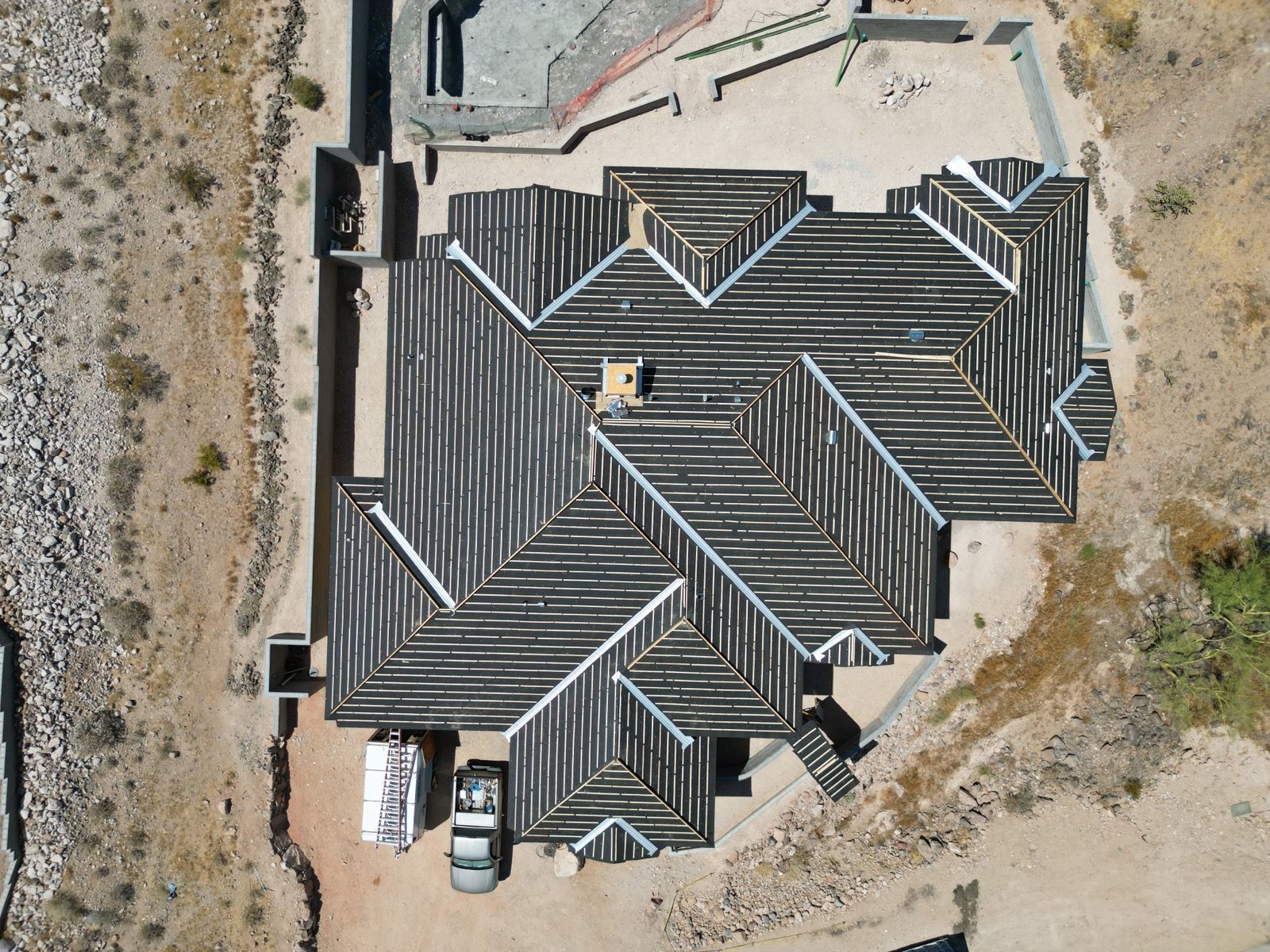 Overhead view of a house with a complex, dark roof in a desert landscape.
