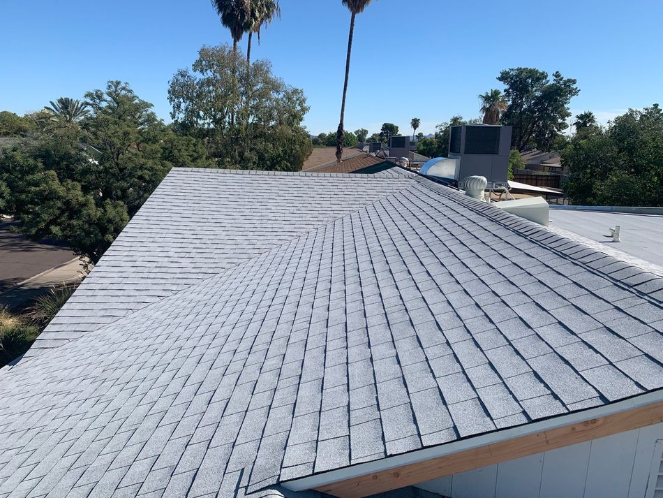 Roofers replacing clay tiles on a house roof under a clear blue sky.