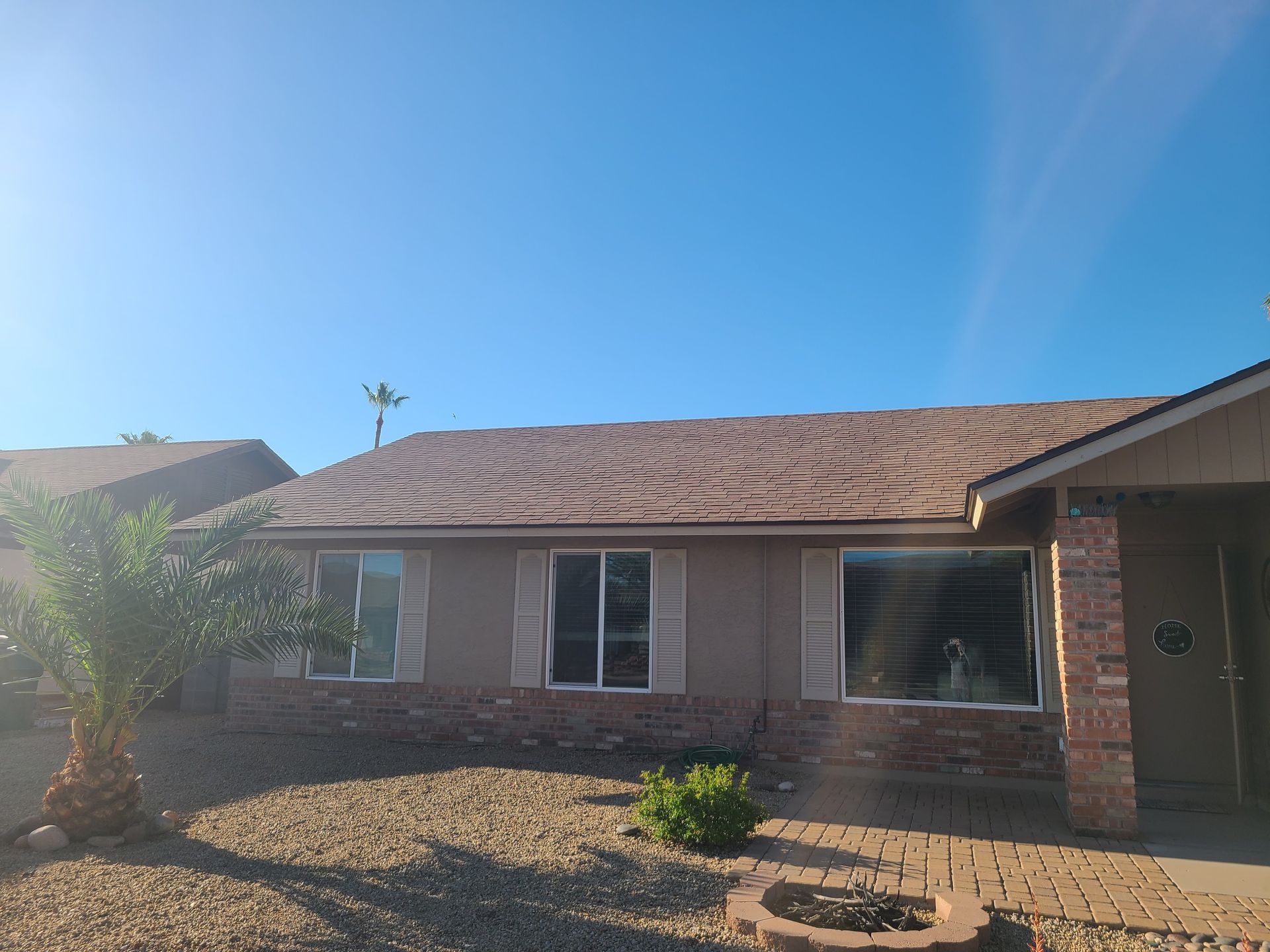 Tan house with brown roof, windows, and small landscaping under a blue sky.
