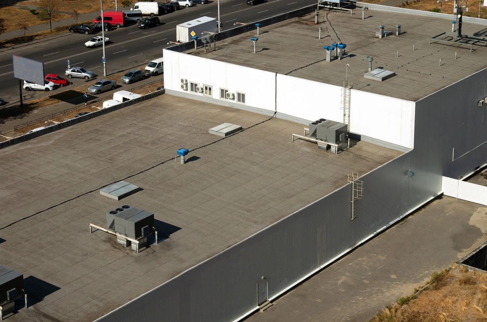 Aerial view of a flat-roofed industrial building with HVAC units and a parking lot nearby.