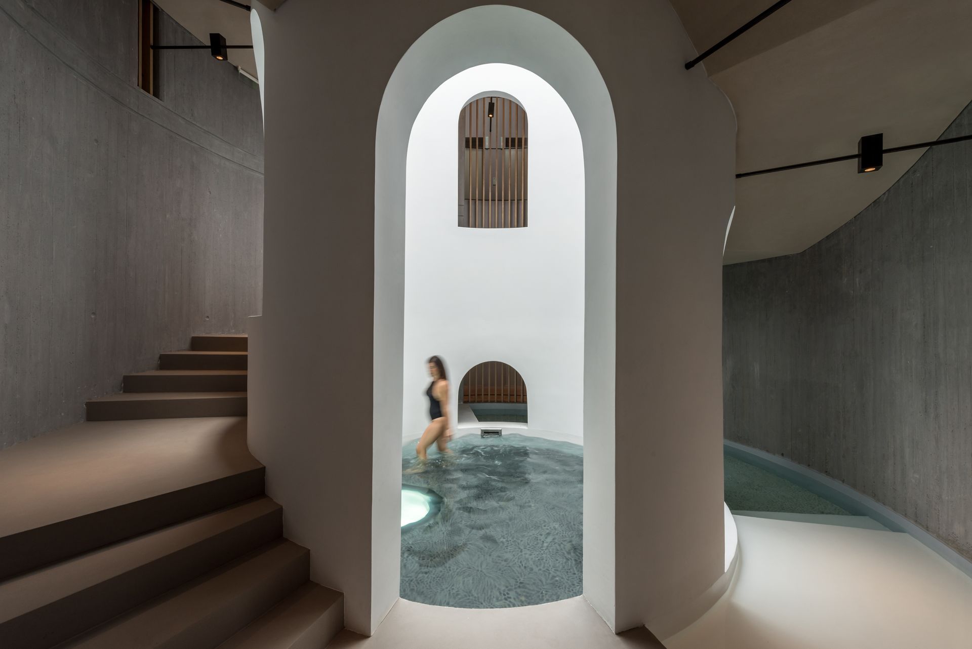Une femme en maillot de bain se tient debout dans une piscine entourée d'escaliers.