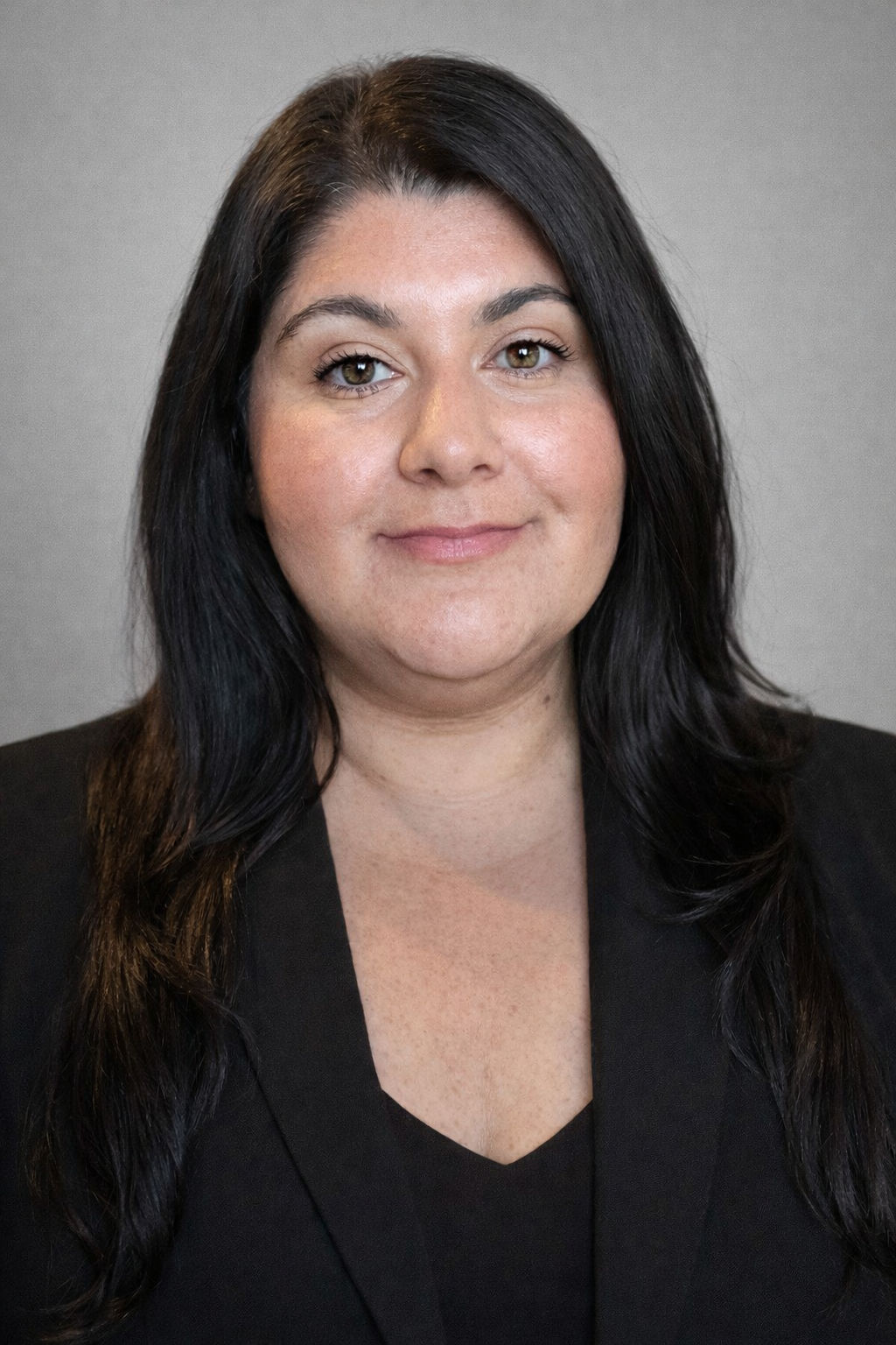 Portrait of a person with long dark hair wearing a black blazer against a gray background