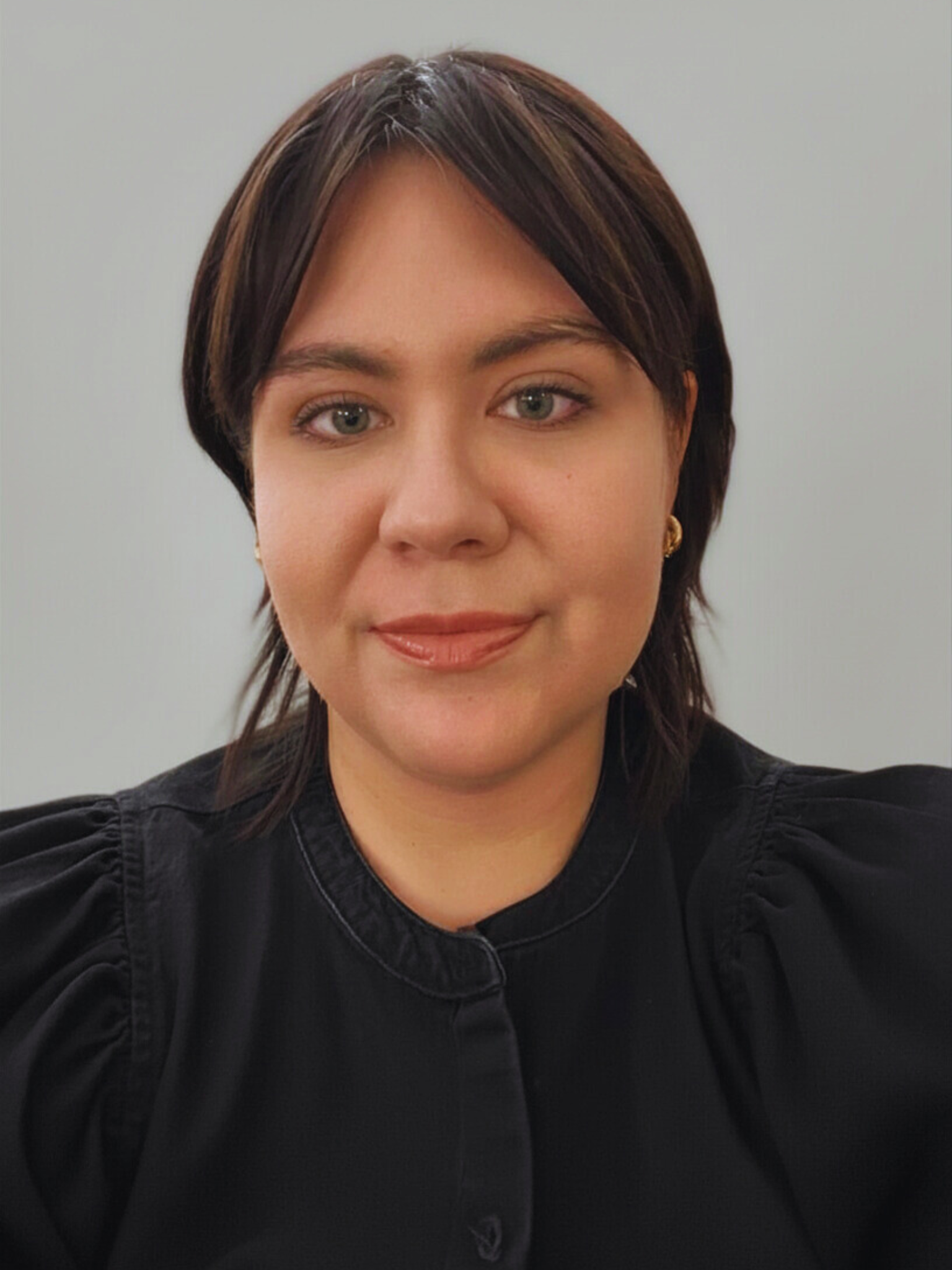 Portrait of a person in a black top against a light gray background, facing forward with a neutral expression