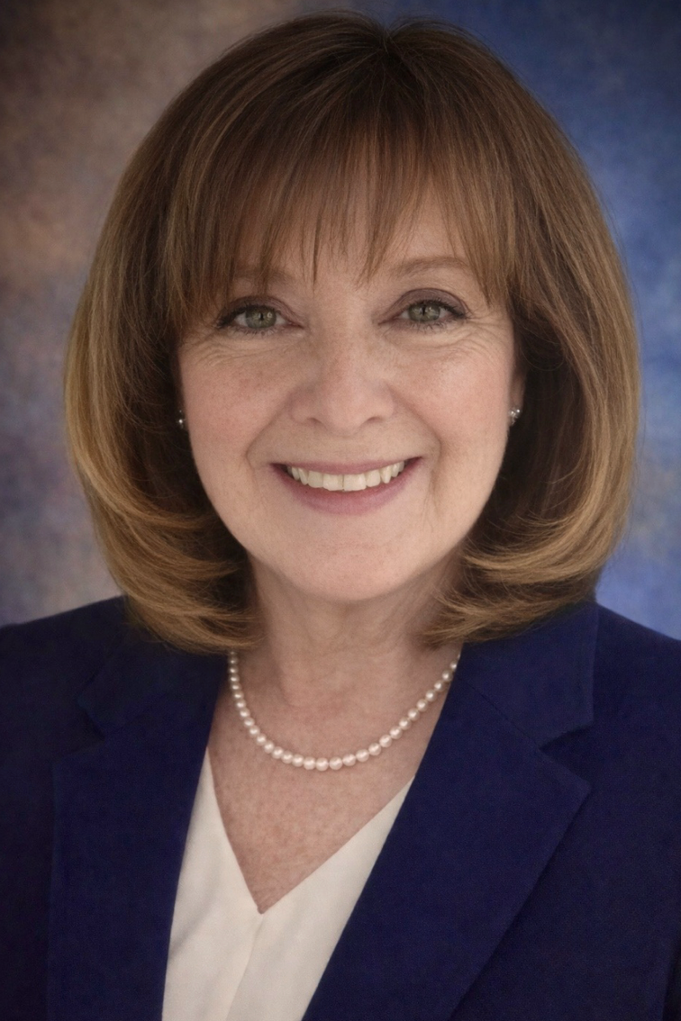 Smiling woman in a navy blazer and pearl necklace against a soft gray studio background