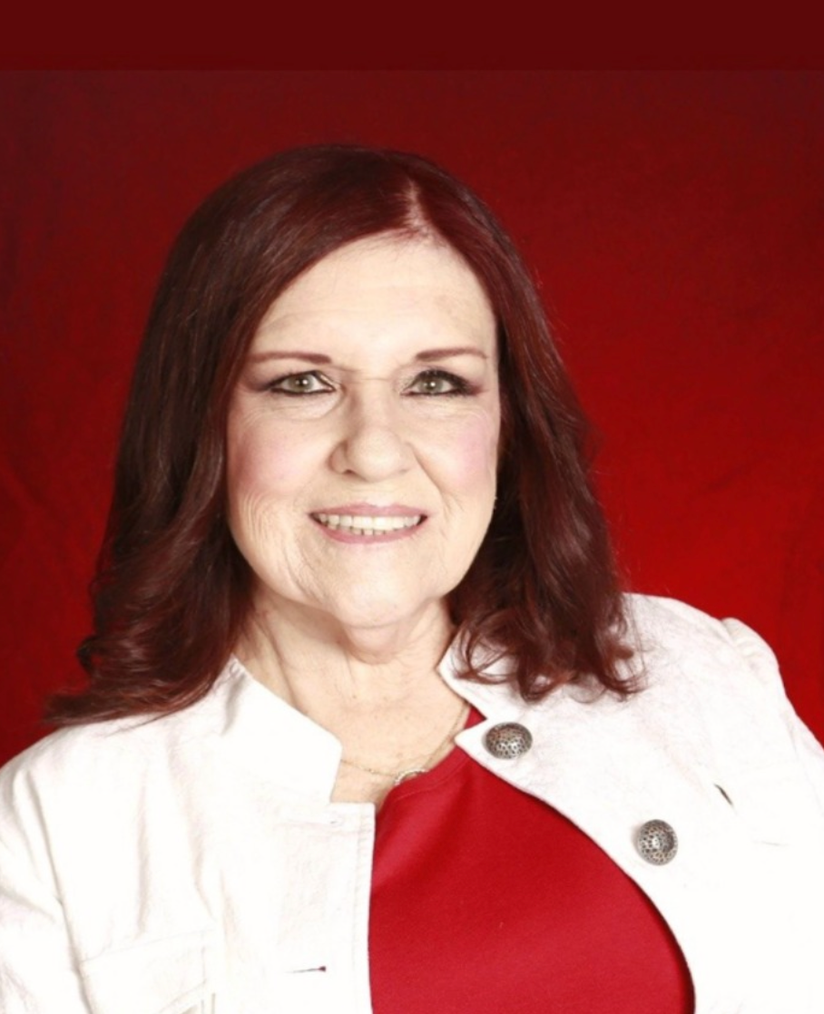 Woman in white jacket over red top, smiling against a red background.