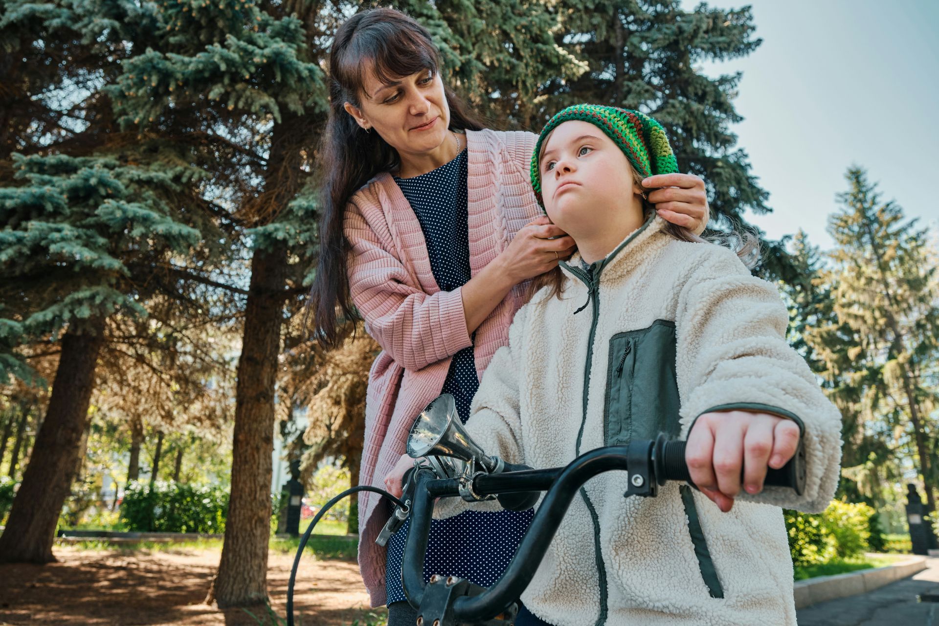 Woman adjusts child’s hat as they stand by a scooter in a sunny park