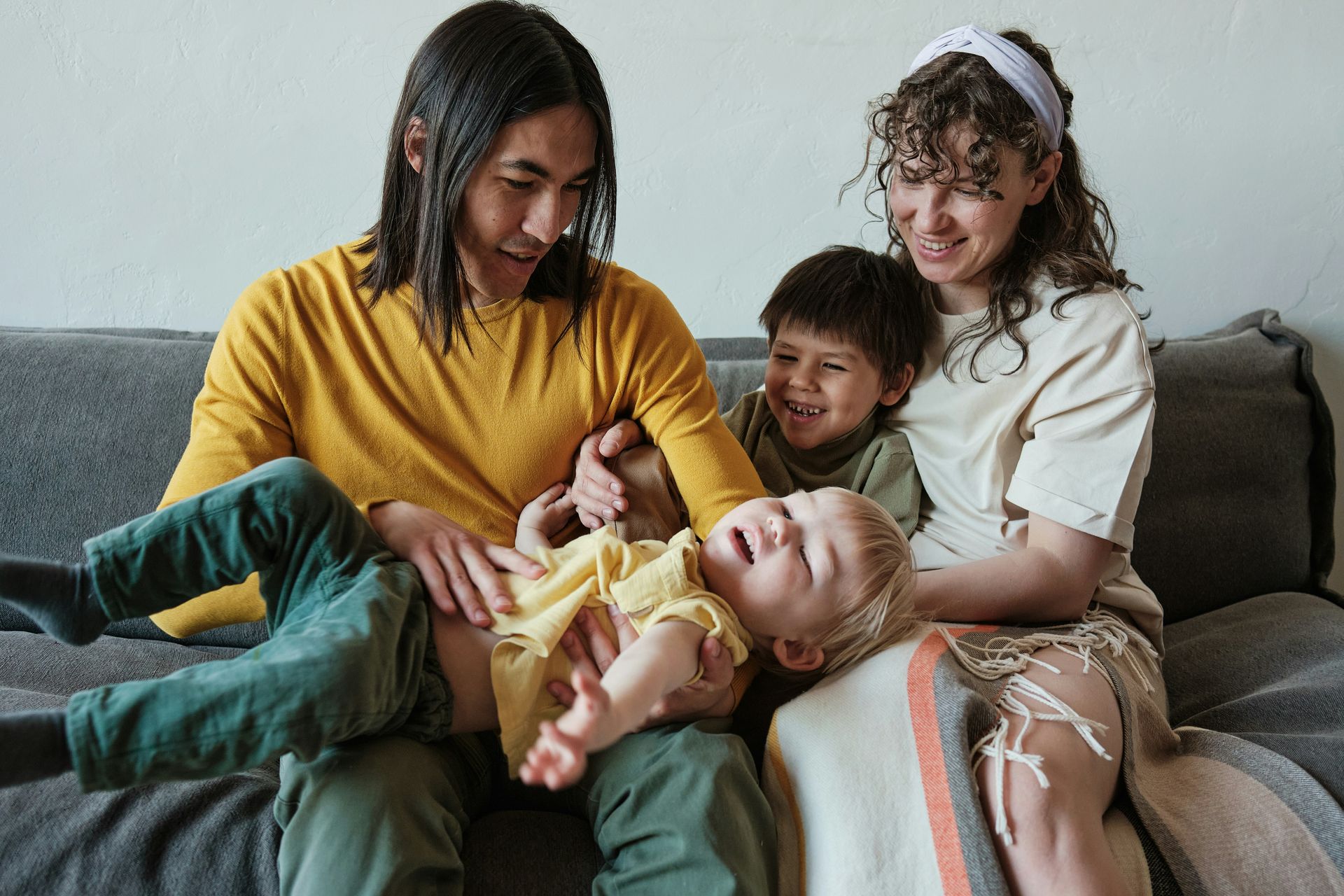 Four people relaxing on a couch, smiling and playing with a child in yellow.