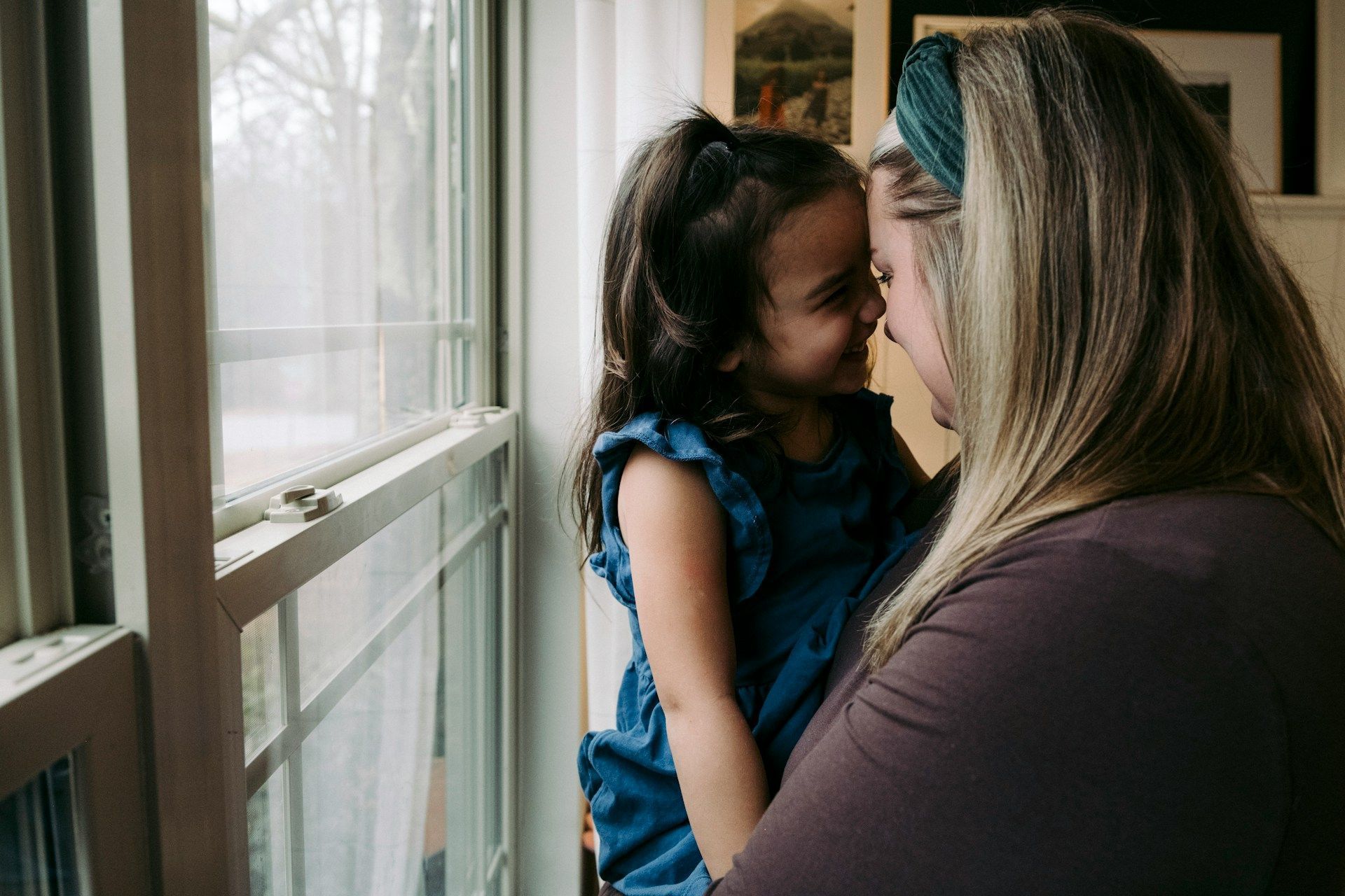 Woman and child by a window, facing each other closely in a quiet moment