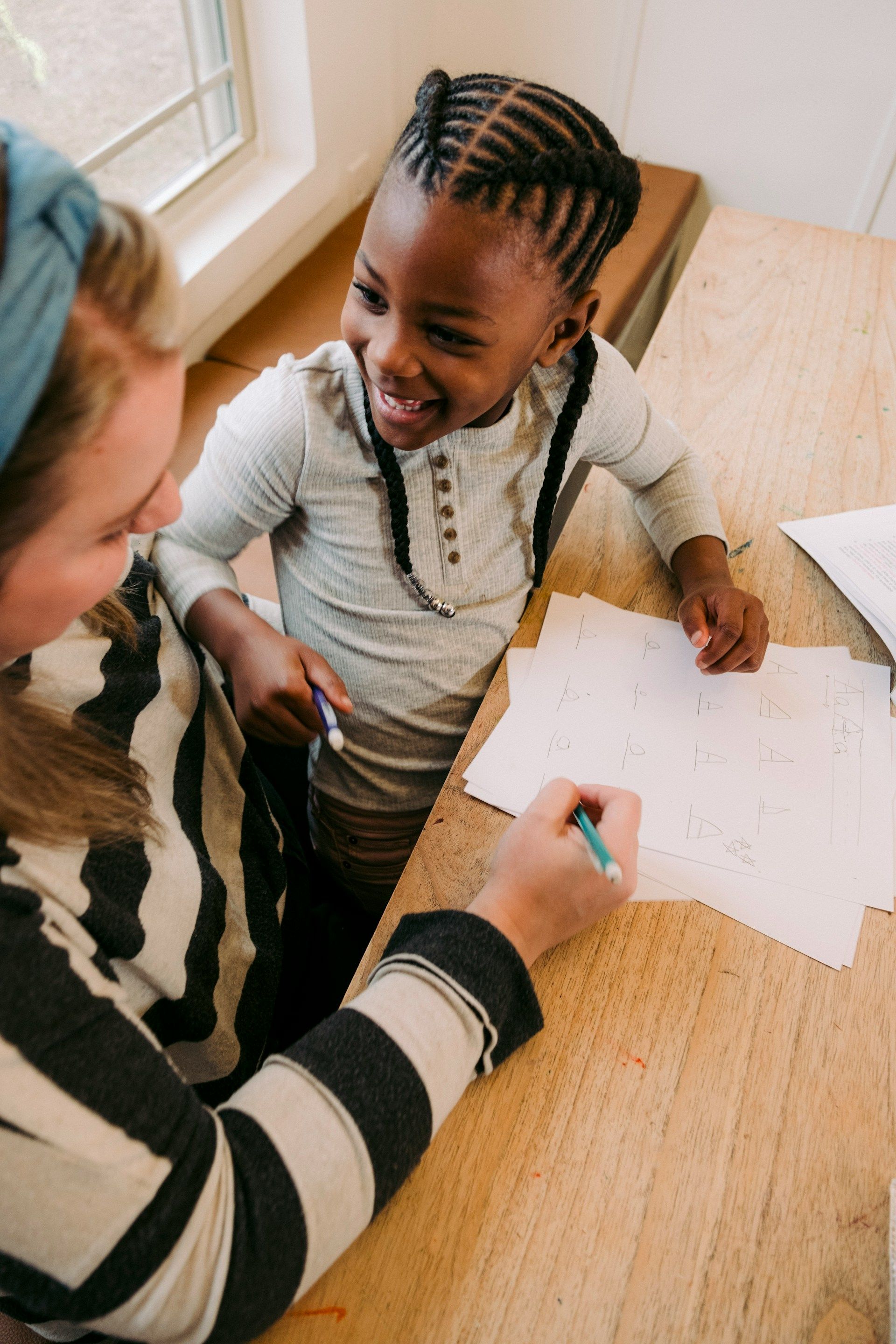 Adult and child smiling at a table, drawing on a sheet of paper with a pencil