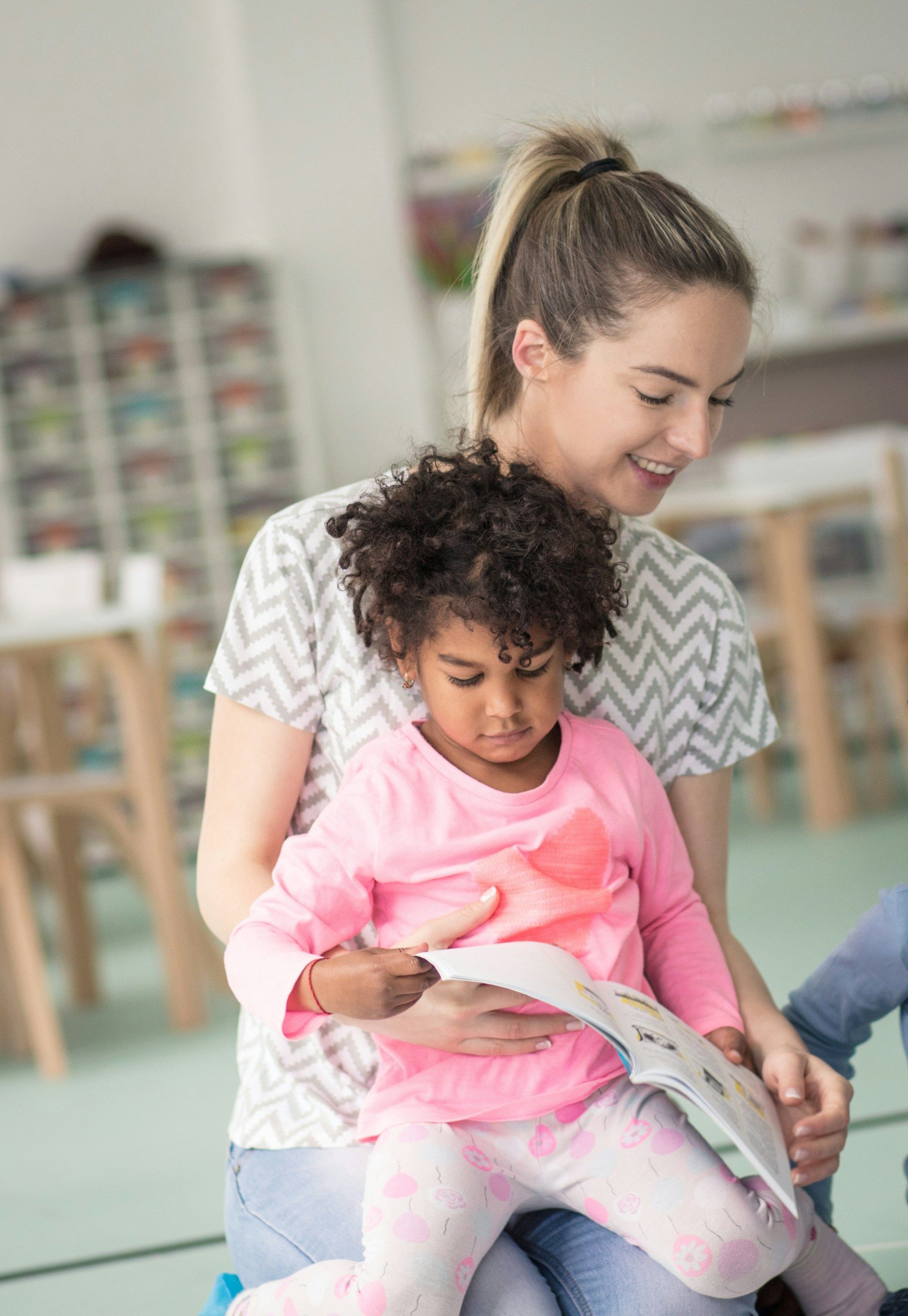Adult holding a child in a bright classroom, both looking at a book together