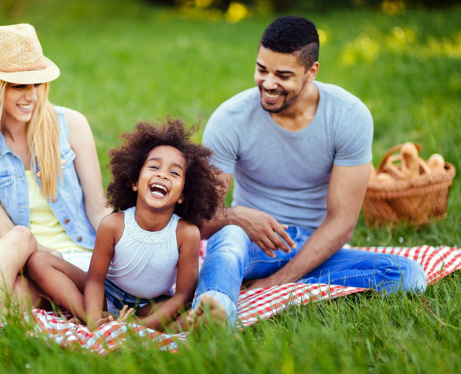 Family laughing on a picnic blanket in a grassy park, with a wicker basket nearby.