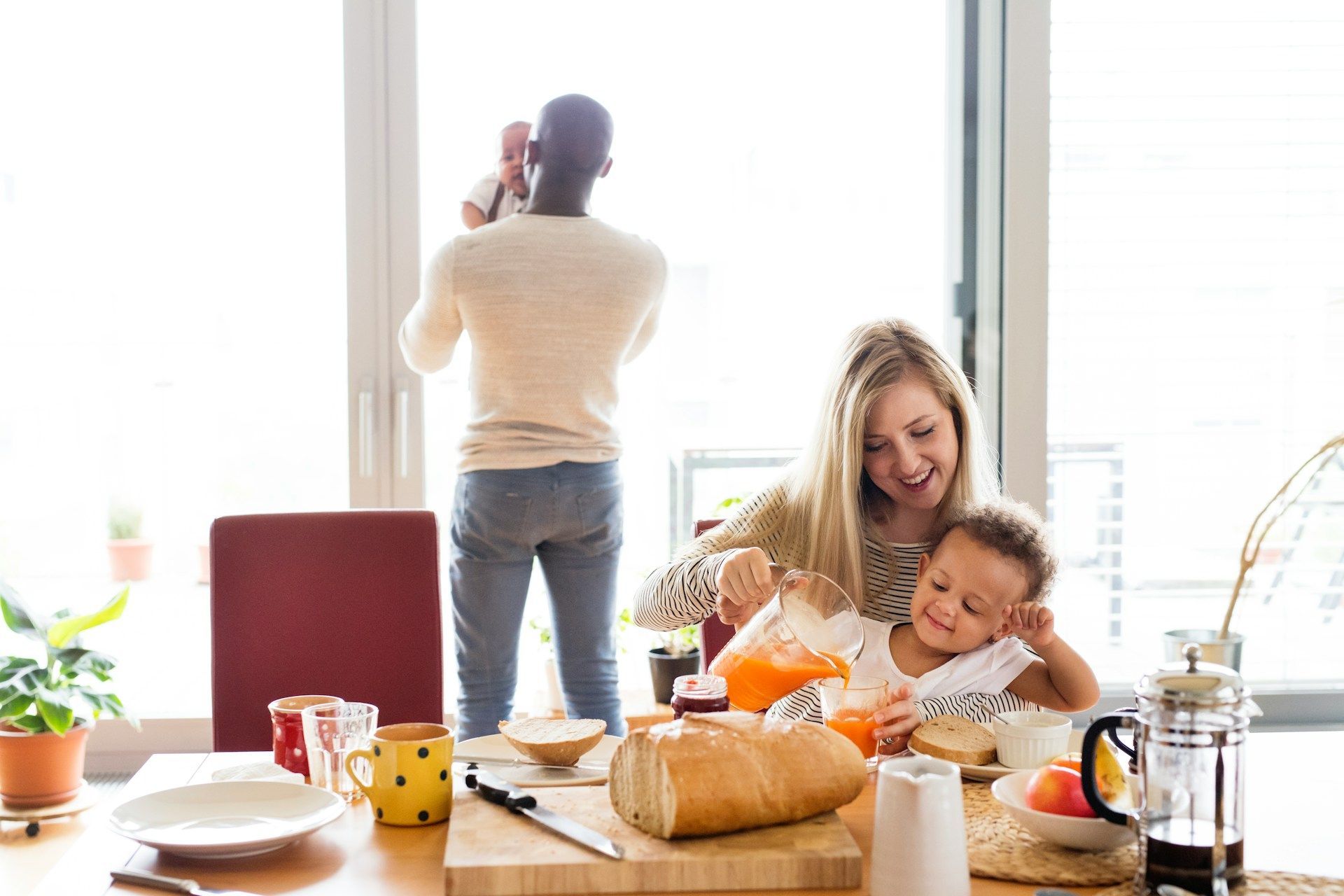 Family cooking in a bright kitchen, with a child and smiling woman at a table and a man standing by the window