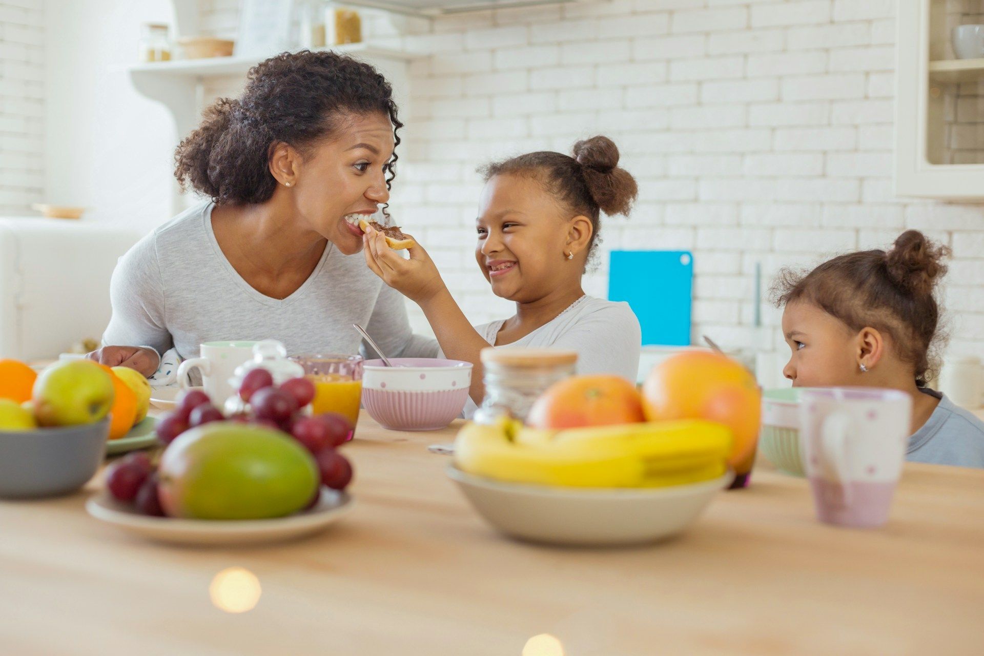 Woman and two children sharing fruit at a kitchen table, smiling together.