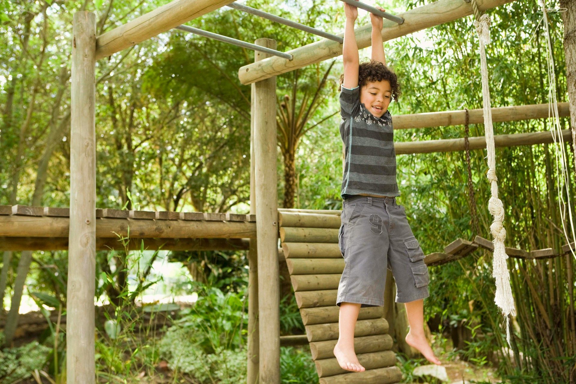 Child hanging from wooden monkey bars in a forest playground