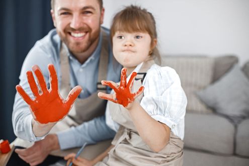 Adult and child showing red painted hands on a couch, smiling at the camera