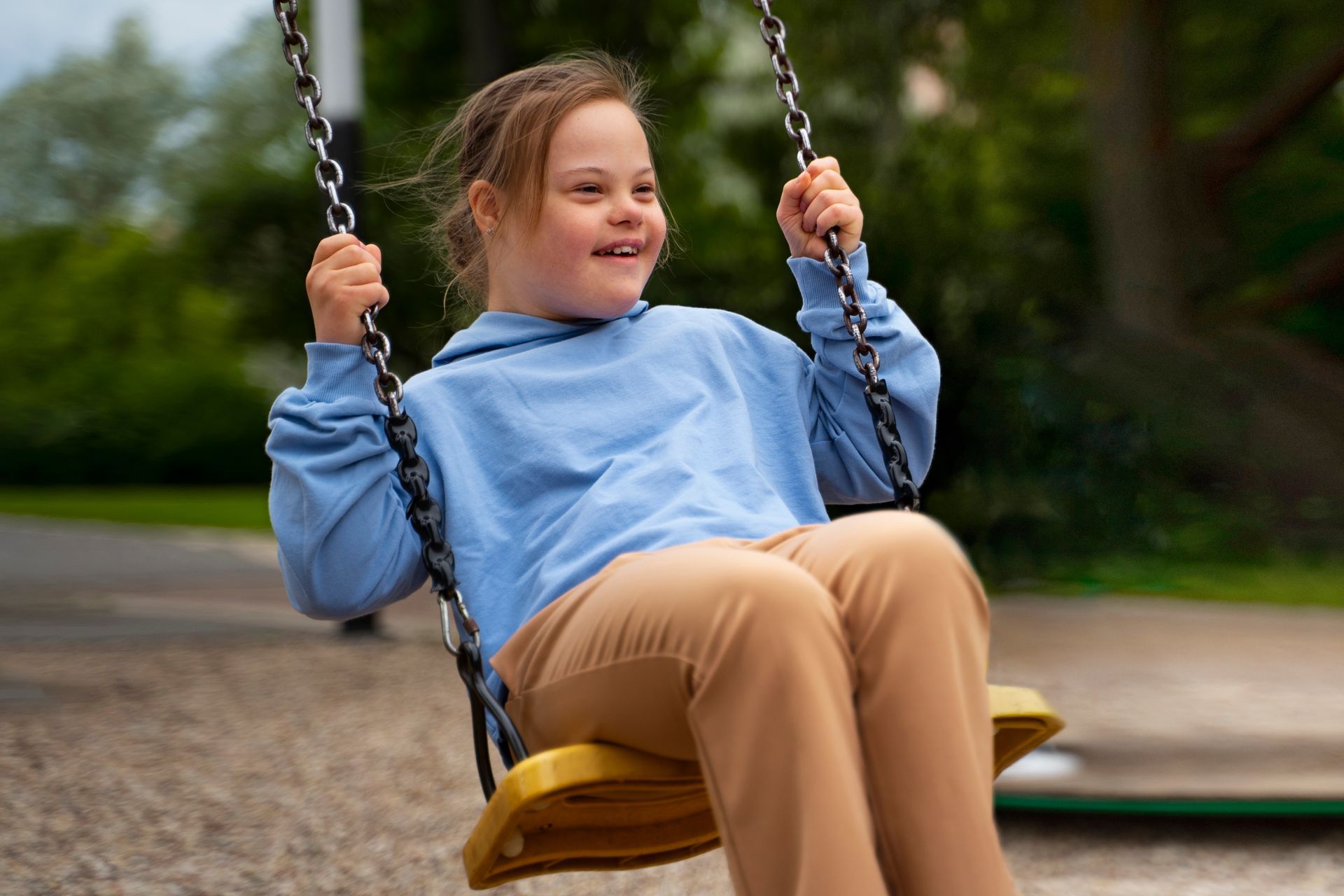 Child in a blue jacket smiling on a swing at a playground.
