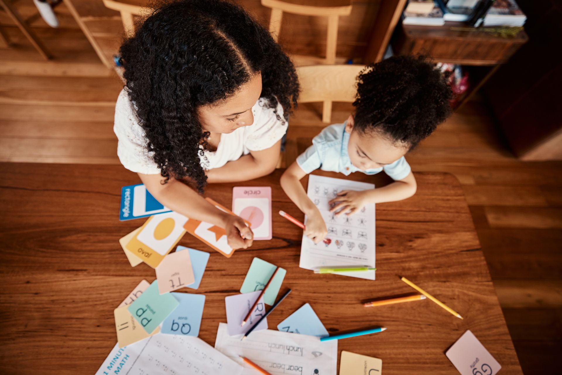 Two children doing a paper craft activity at a wooden table with colorful cutout cards and pencils