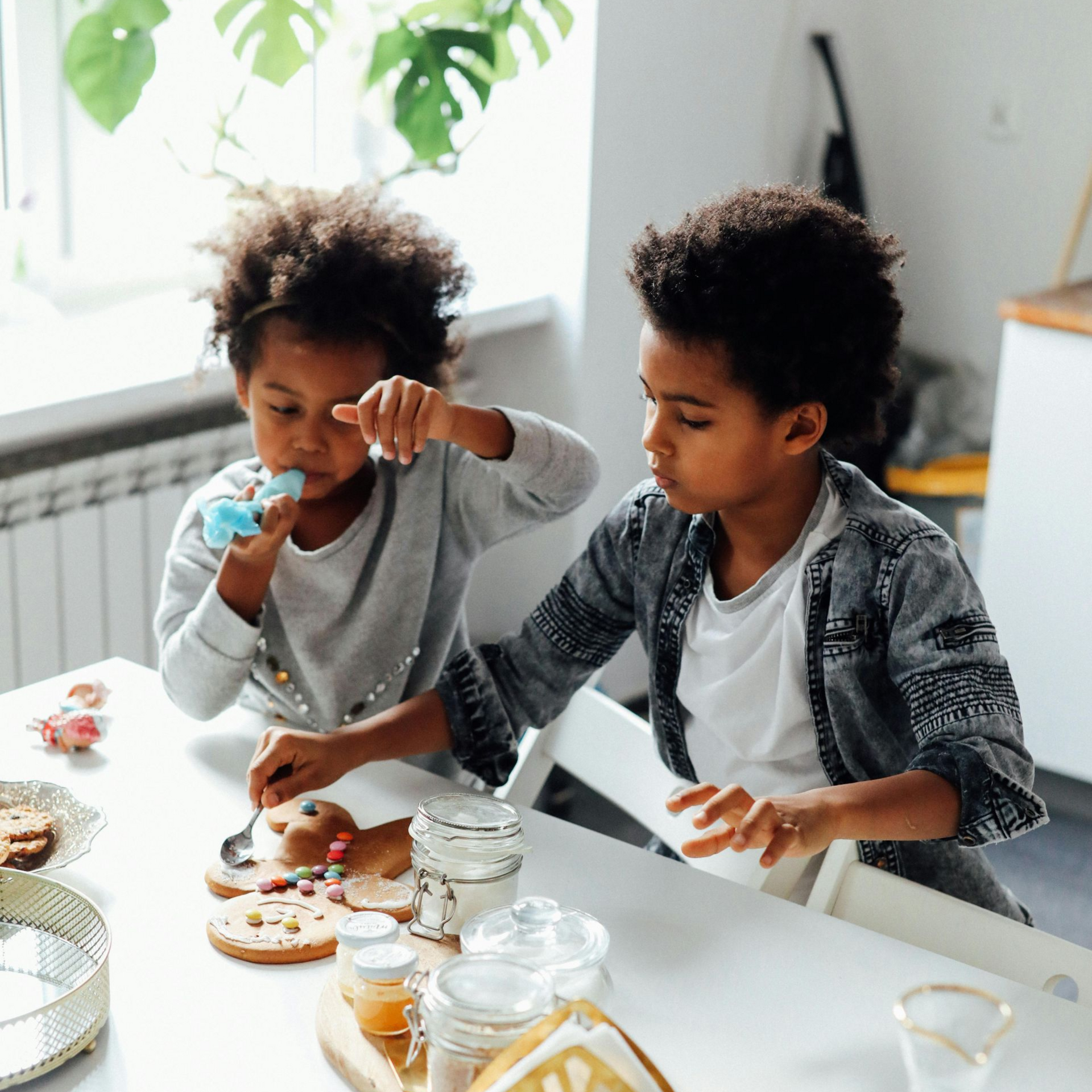 Two children decorating cupcakes at a white table in a bright kitchen