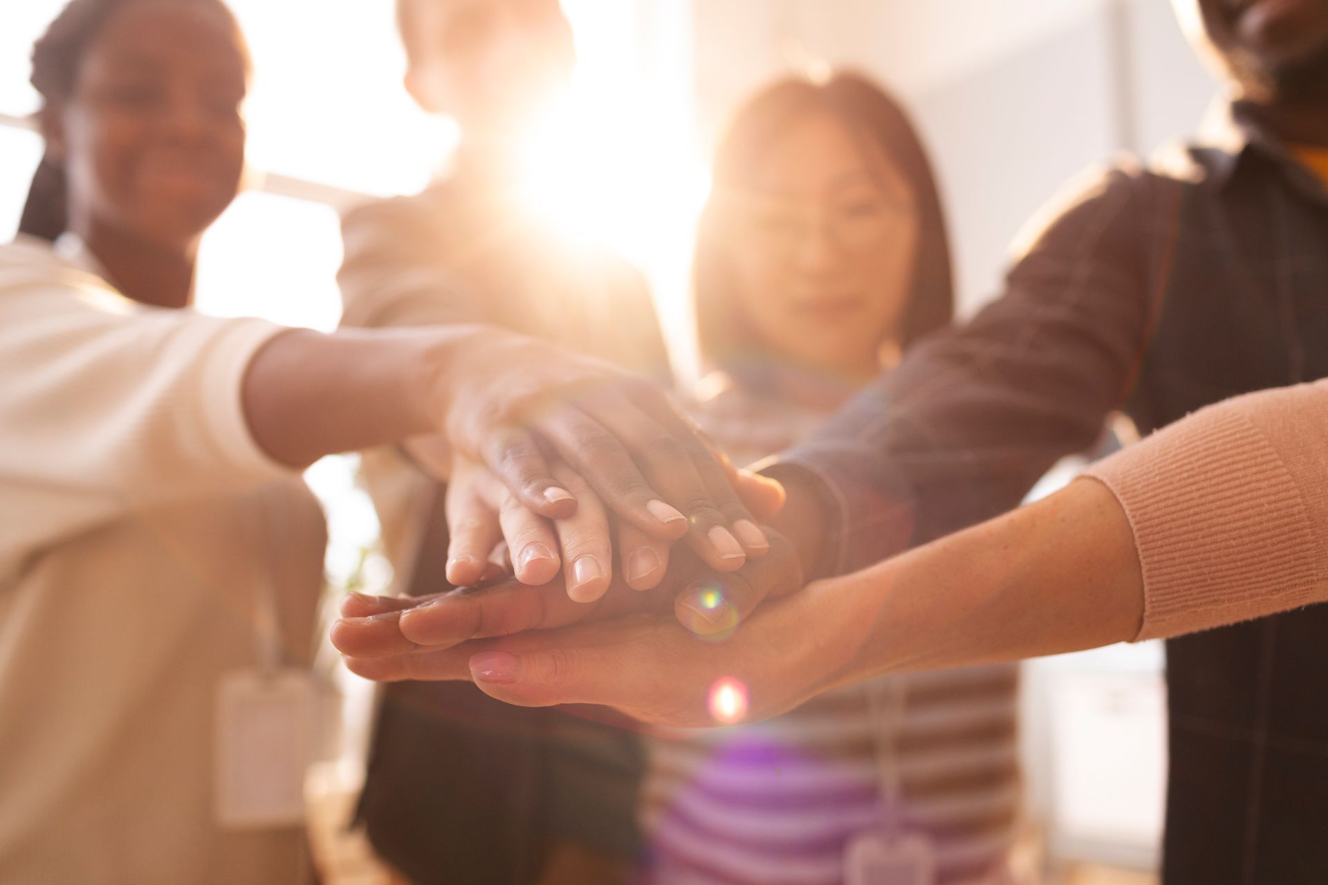 Hands stacked together in a team huddle with warm sunlight in the background